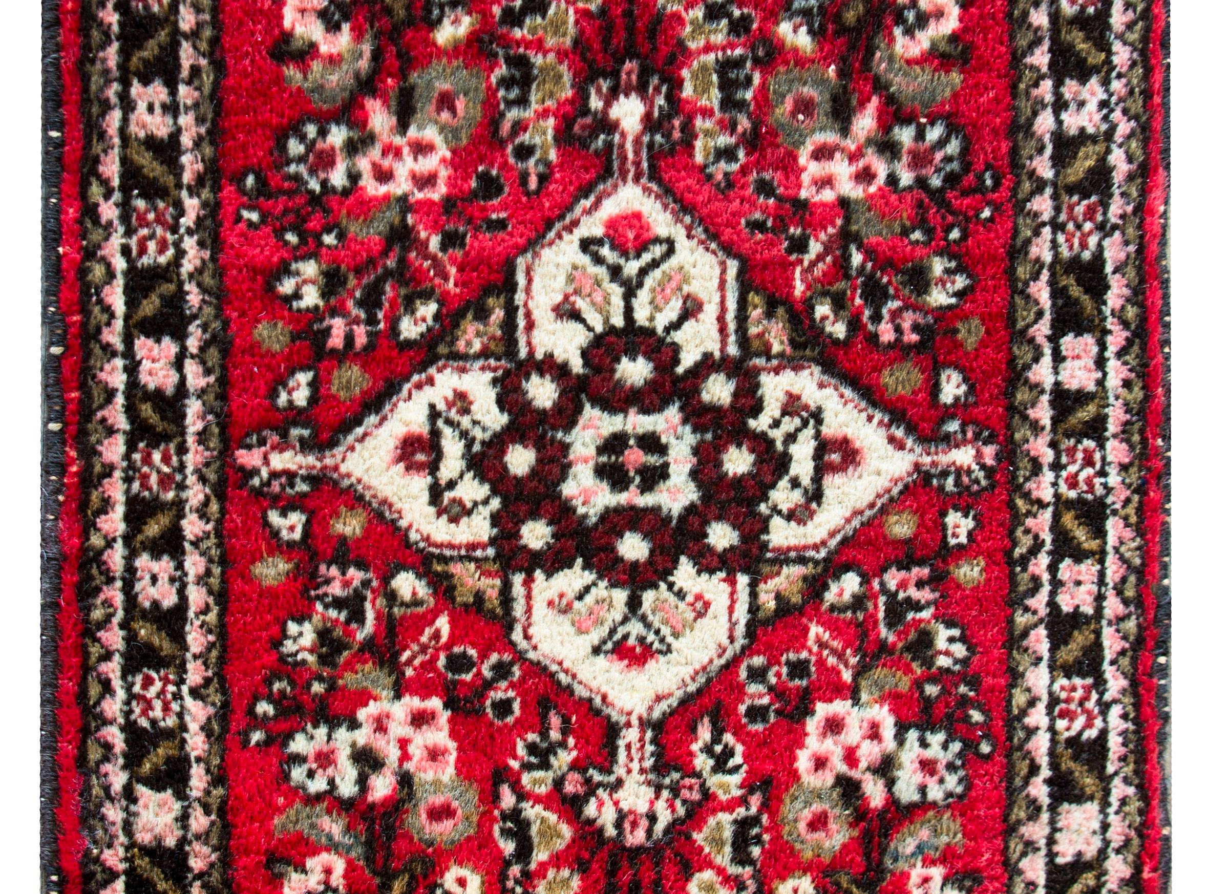 A sweet mid-20th century Persian Hamadan rug with a central floral medallion living amidst a densely woven field of more flowers, all woven in pinks, white, black, and taupe on a cranberry background, and surrounded by a border with petite floral