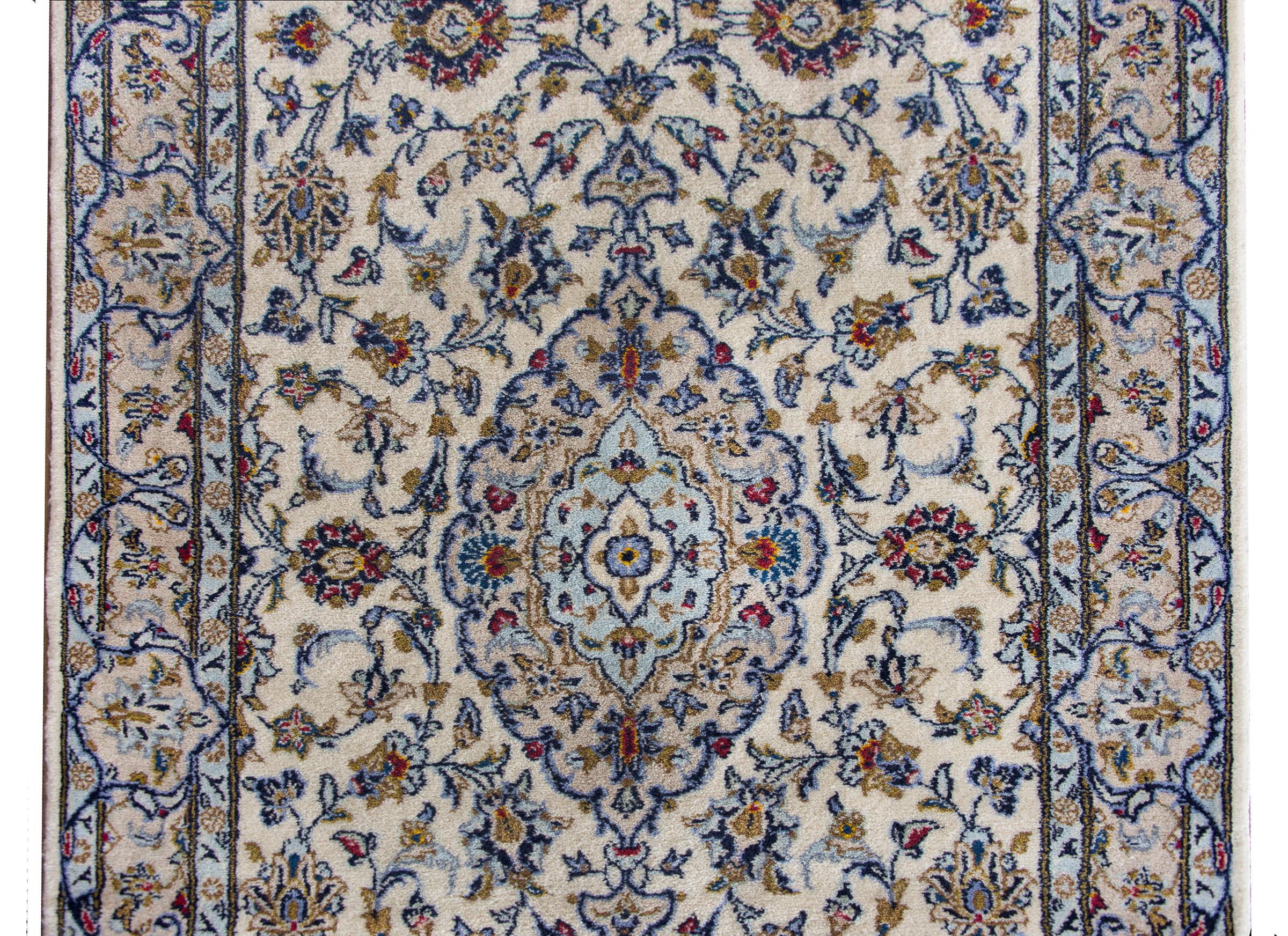 A beautiful mid-20th century Persian Kashan runner with a four large floral medallions living amidst a field of even more scrolling vines and flowers, all woven in crimson, gold, light and dark indigo, and set against a white background.  The border