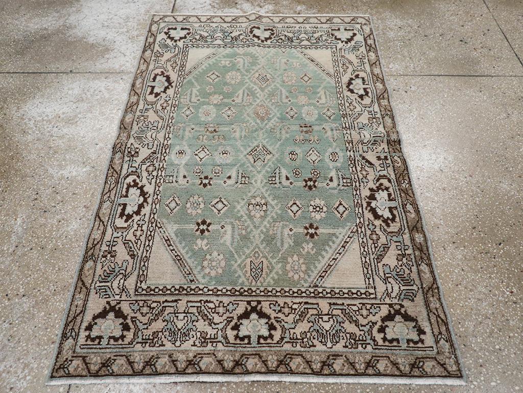 Ein Wollflor aus symmetrischen Knoten auf einer Baumwollunterlage. Das hell schiefergraue Feld zeigt eine Malayer-Variante des Allover-Herati-Musters mit einer zentralen Säule aus aneinandergereihten, gefransten Rauten, flankiert von den üblichen