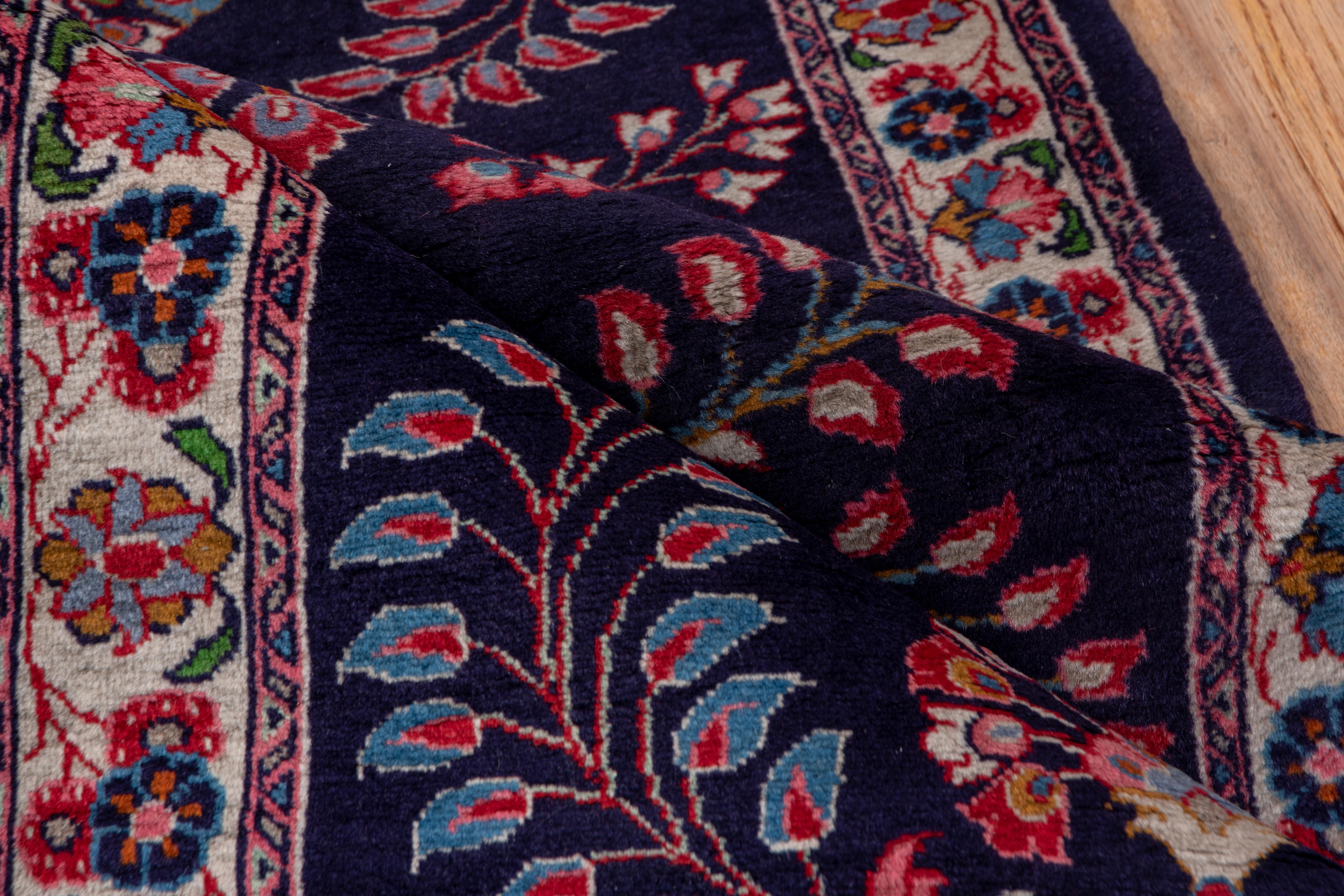 This well drawn and balanced West Persian small runner shows a navy blue field decorated with curvaceous leaf and bud sprays centered by a small octogramme and four radiating floral motives. Red and teal accents. Ecru border with rosettes and