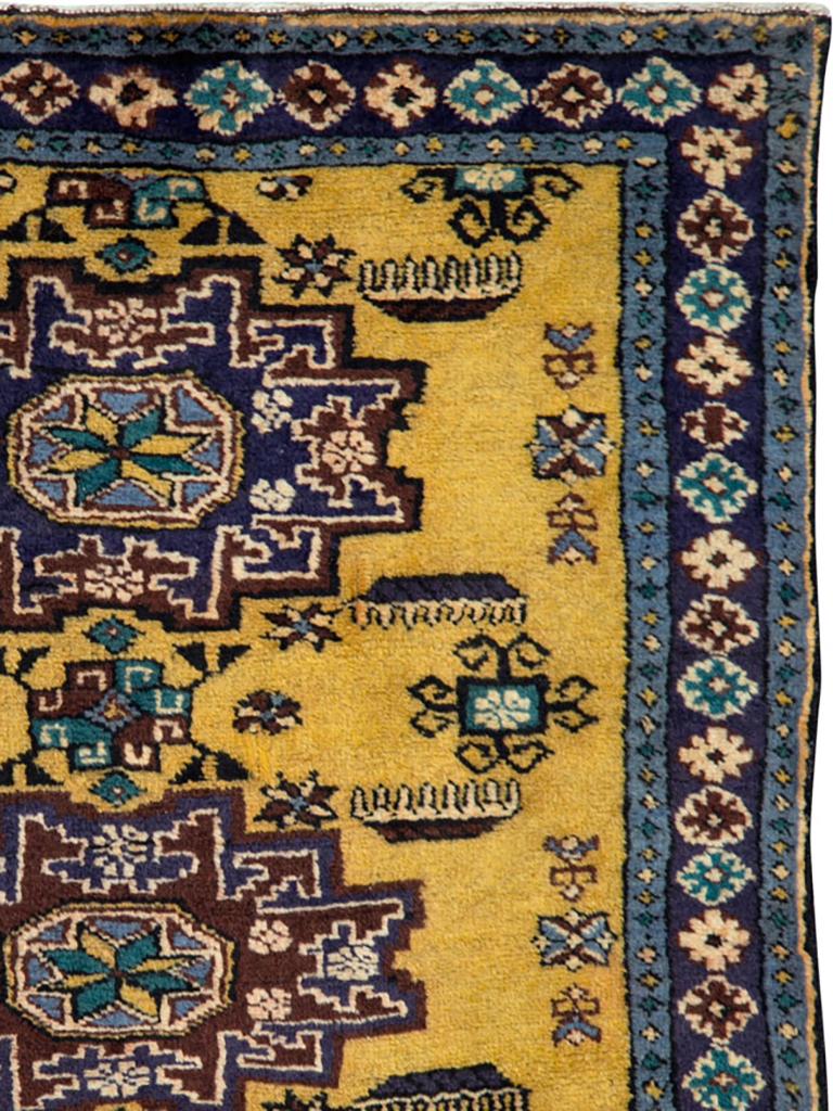The golden yellow field supports three closely stacked 12 point “Lesghi stars” with attendant stylized horizontal leaves and small rams horned squares. Navy border of colorful rosettes. Wool warp. Probably Kuba/Caucasian origin. Medium weave with