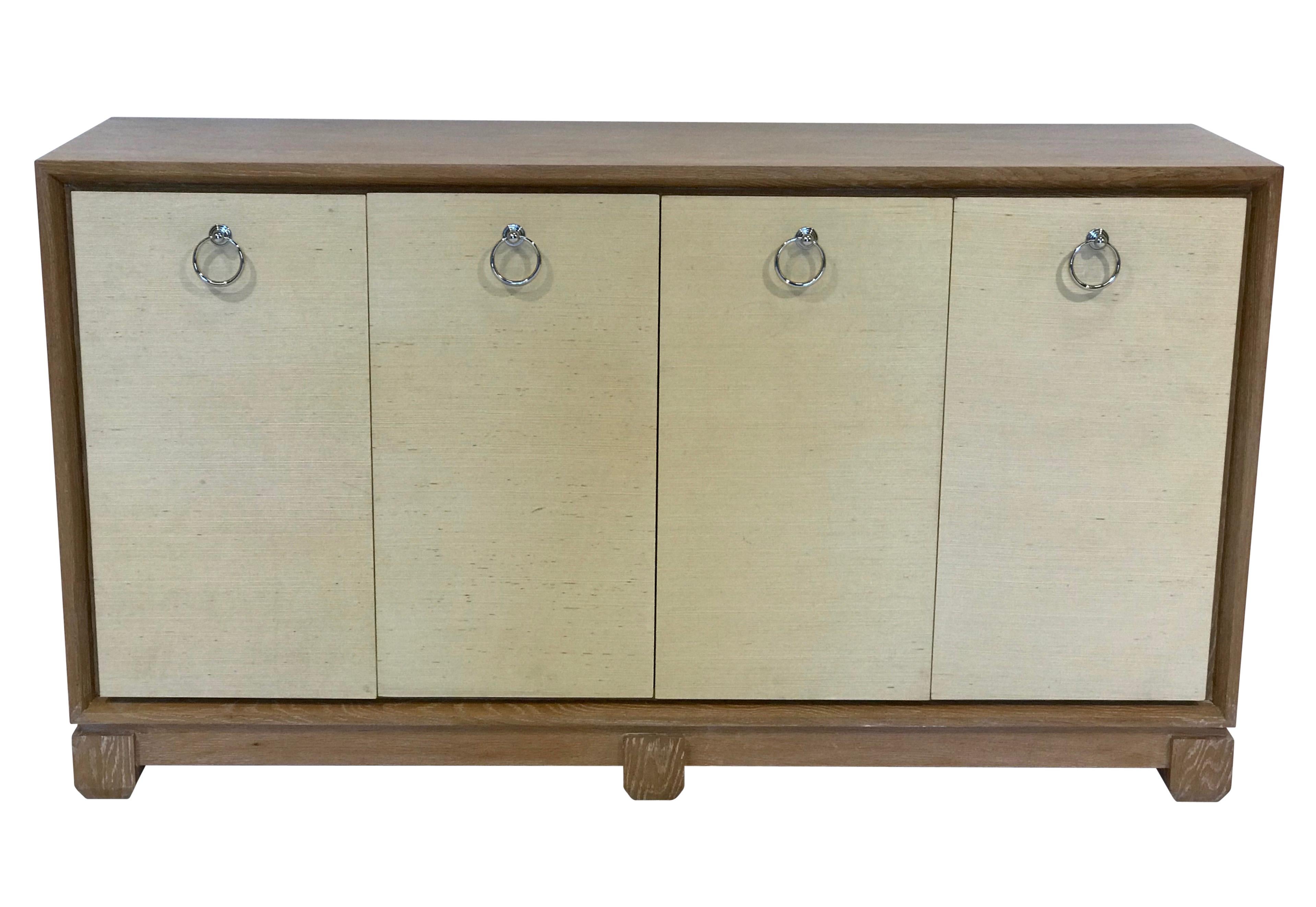 Beautifully constructed American contemporary solid pickled oak credenza having a natural woven fabric covering the front doors and on the interior.  Fitted interior shelves and chrome ring handles on the door fronts. 

