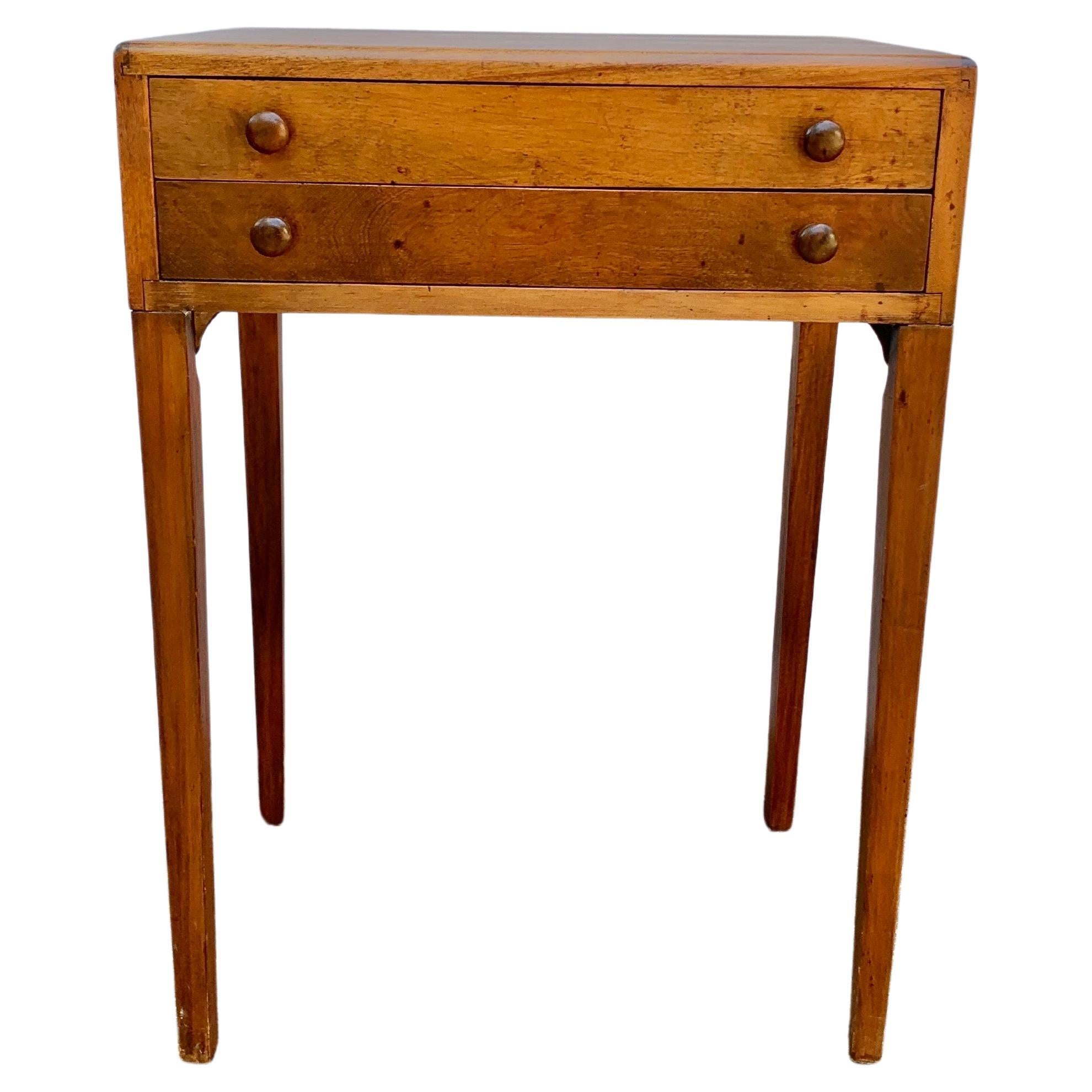 This Mid 20th Century Side Table was crafted from white Pine in the mid 1900's. The piece features a chest style top containing two slender drawers restng on four tapered legs. Each of the two drawers retain their original wood pulls. This Mid 20th
