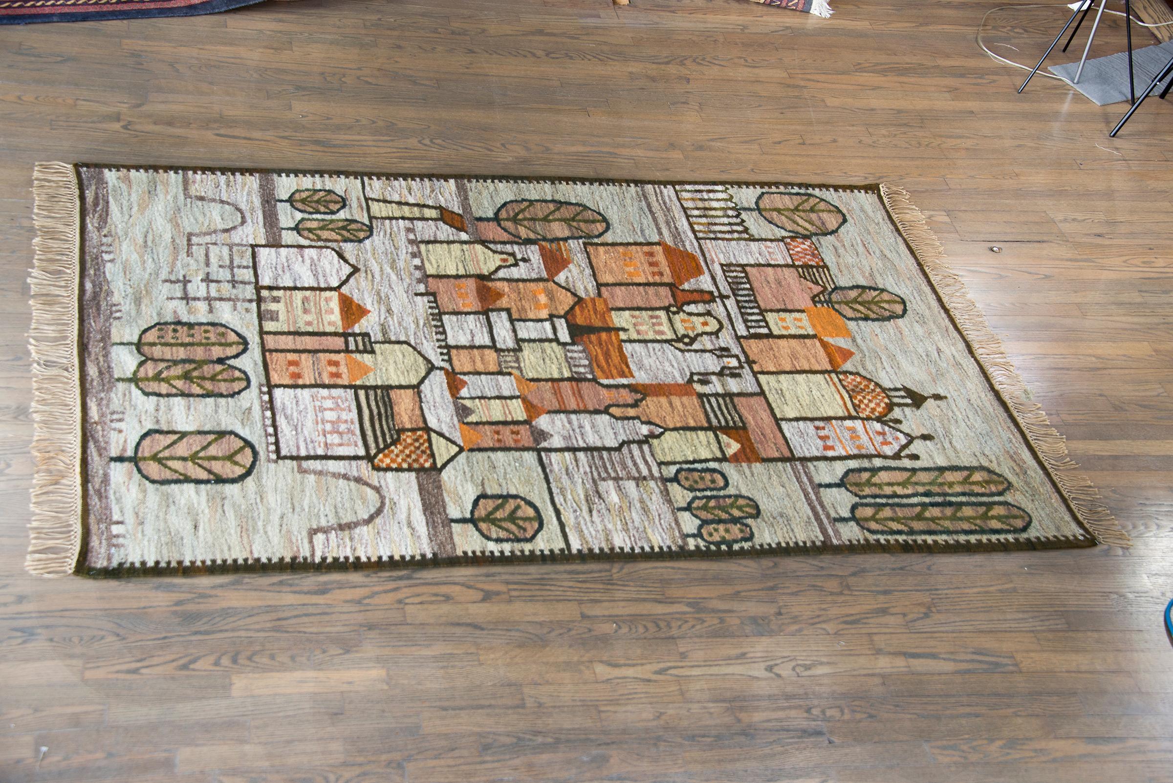 A beautiful mid-20th century Polish Folk Art Cepelia rug depicting a village with rows of houses and churches, and sylized trees, all woven in muted orange, yellows, creams, greens, and browns.  Cepelia rugs were a luxury commodity made during the