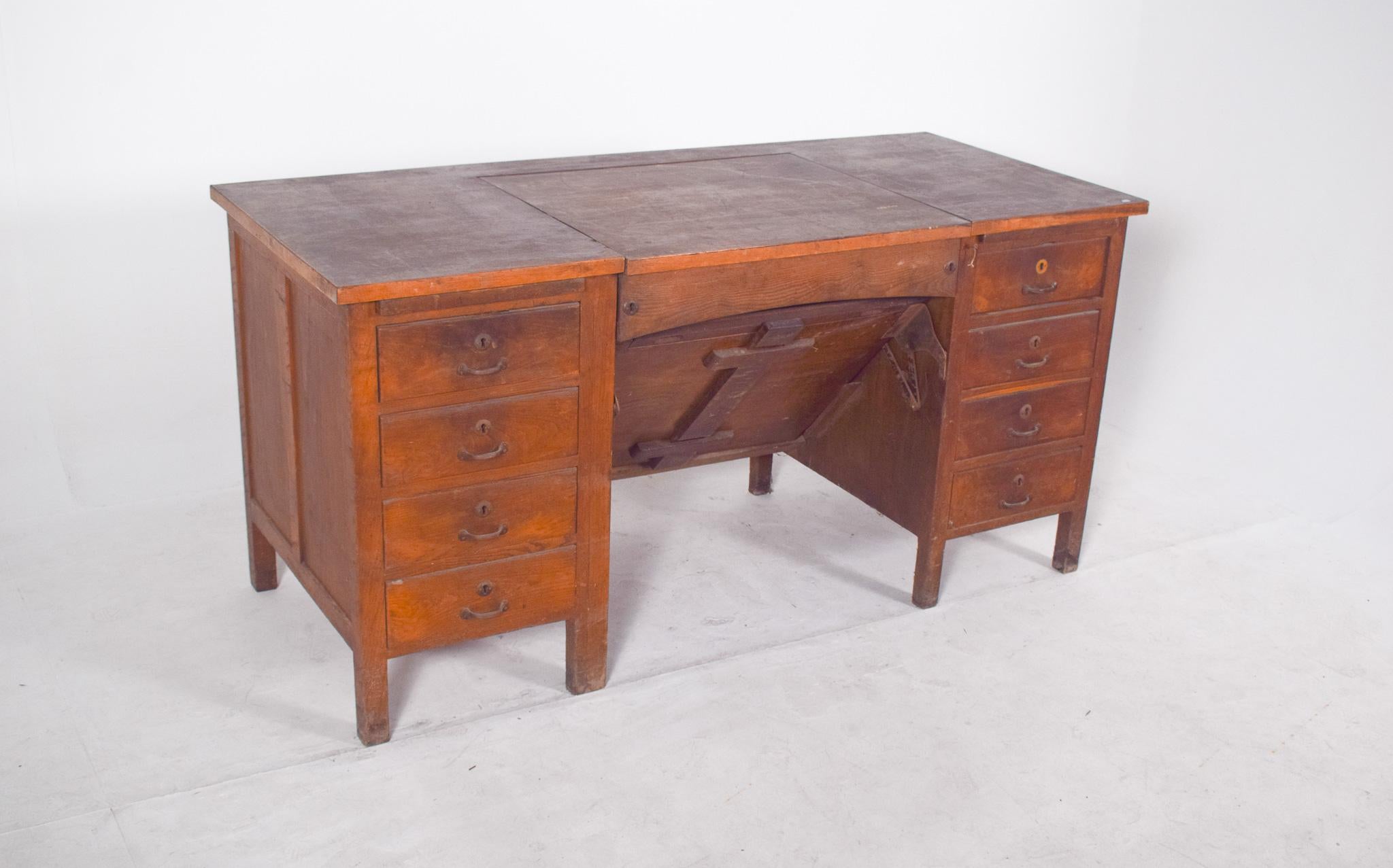 Scrivania portoghese della metà del XX secolo con piano inclinabile. Il suo design funzionale è tipico degli anni '30 e '50. Il pezzo presenta una struttura simmetrica con dieci cassetti, cinque per lato, con maniglie in metallo e fori per le