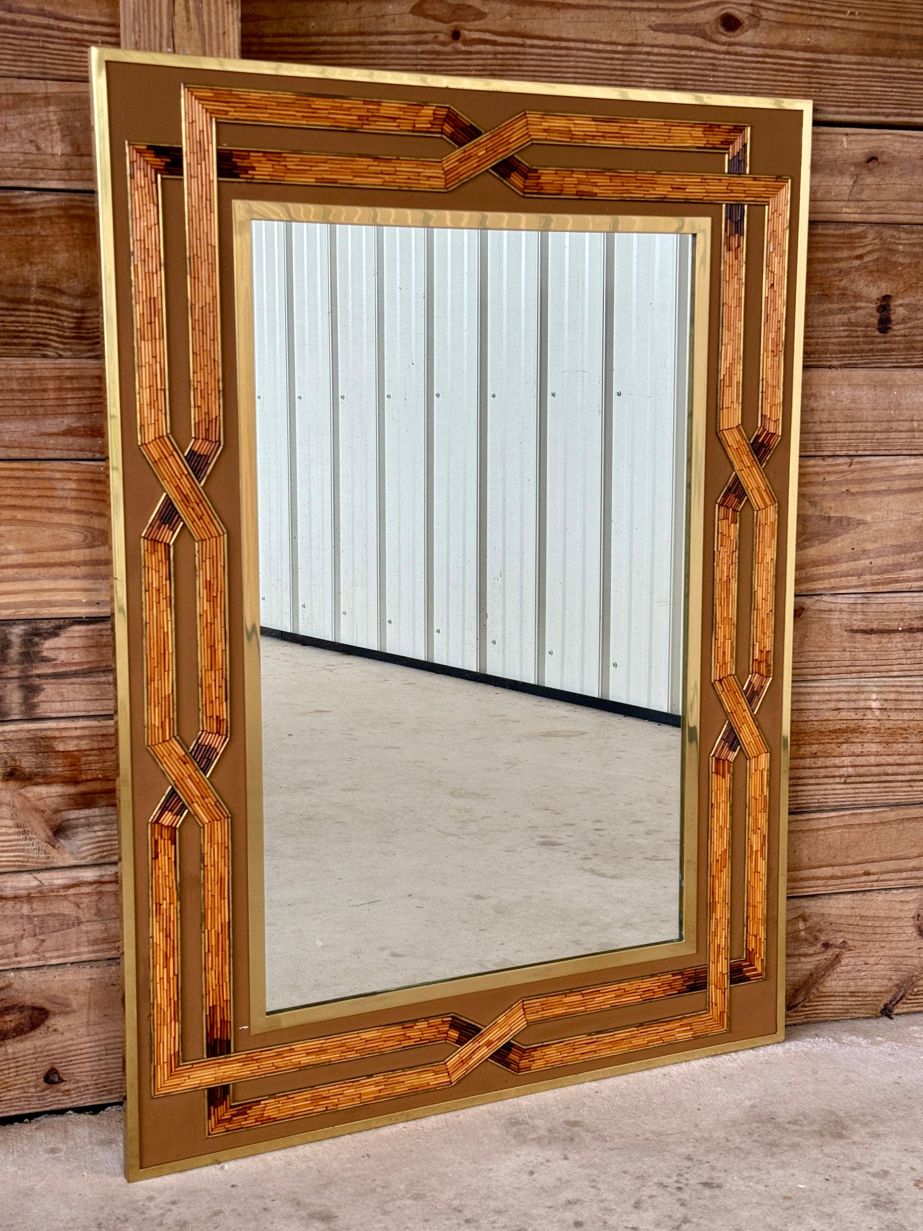 Ce superbe miroir du milieu du XXe siècle présente un cadre en laiton complexe orné d'incrustations de rotin méticuleusement disposées, créant un design géométrique et stratifié rappelant l'esthétique emblématique de Gabriella Crespi ou Karl