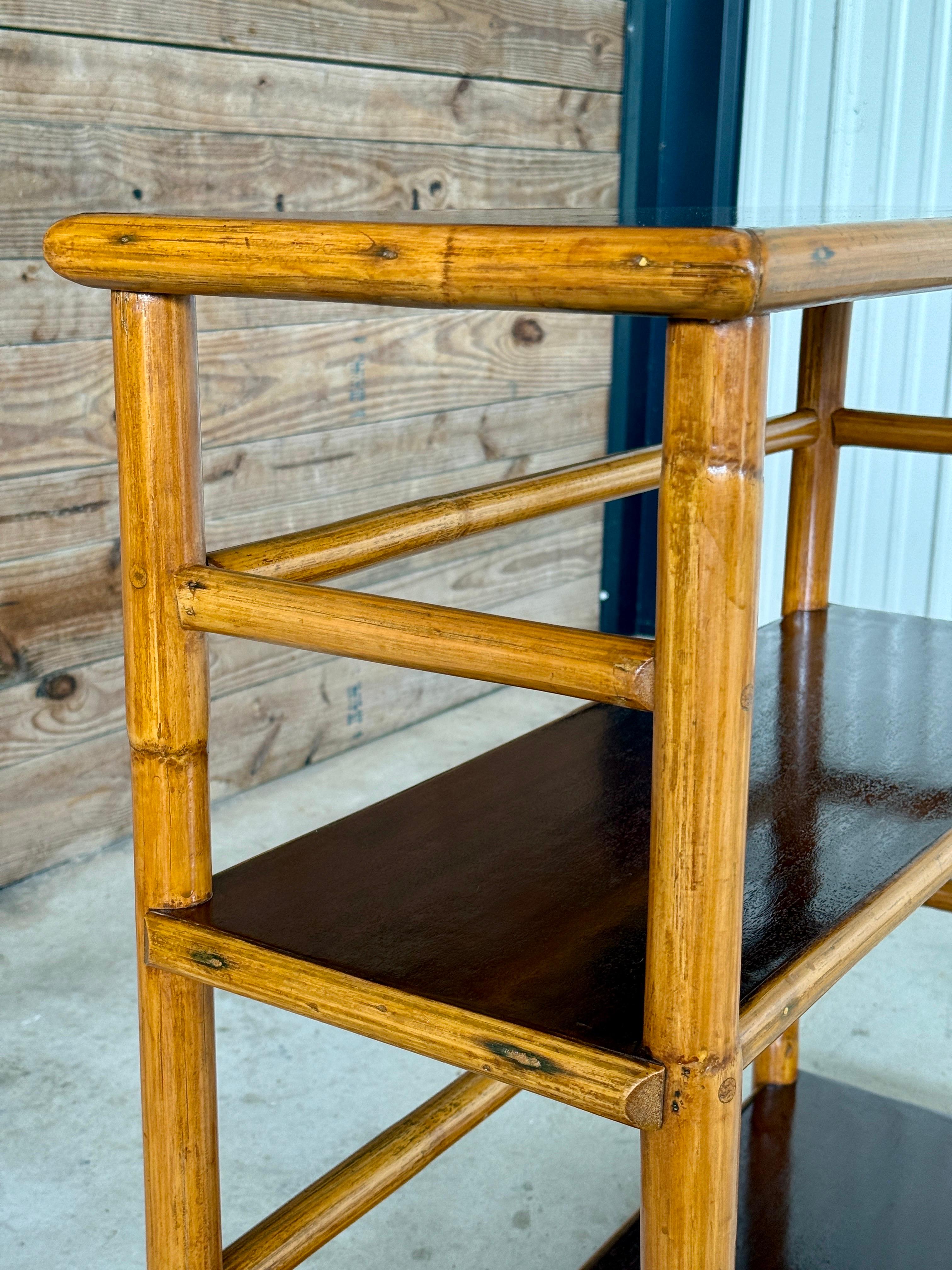 A classic Mid-20th Century rattan bookshelf by Ritts Tropitan, the pioneering California company known for its sleek tropical-modern designs. This three-tier shelf features a sturdy rattan frame and rich mahogany-toned shelves, recently refinished