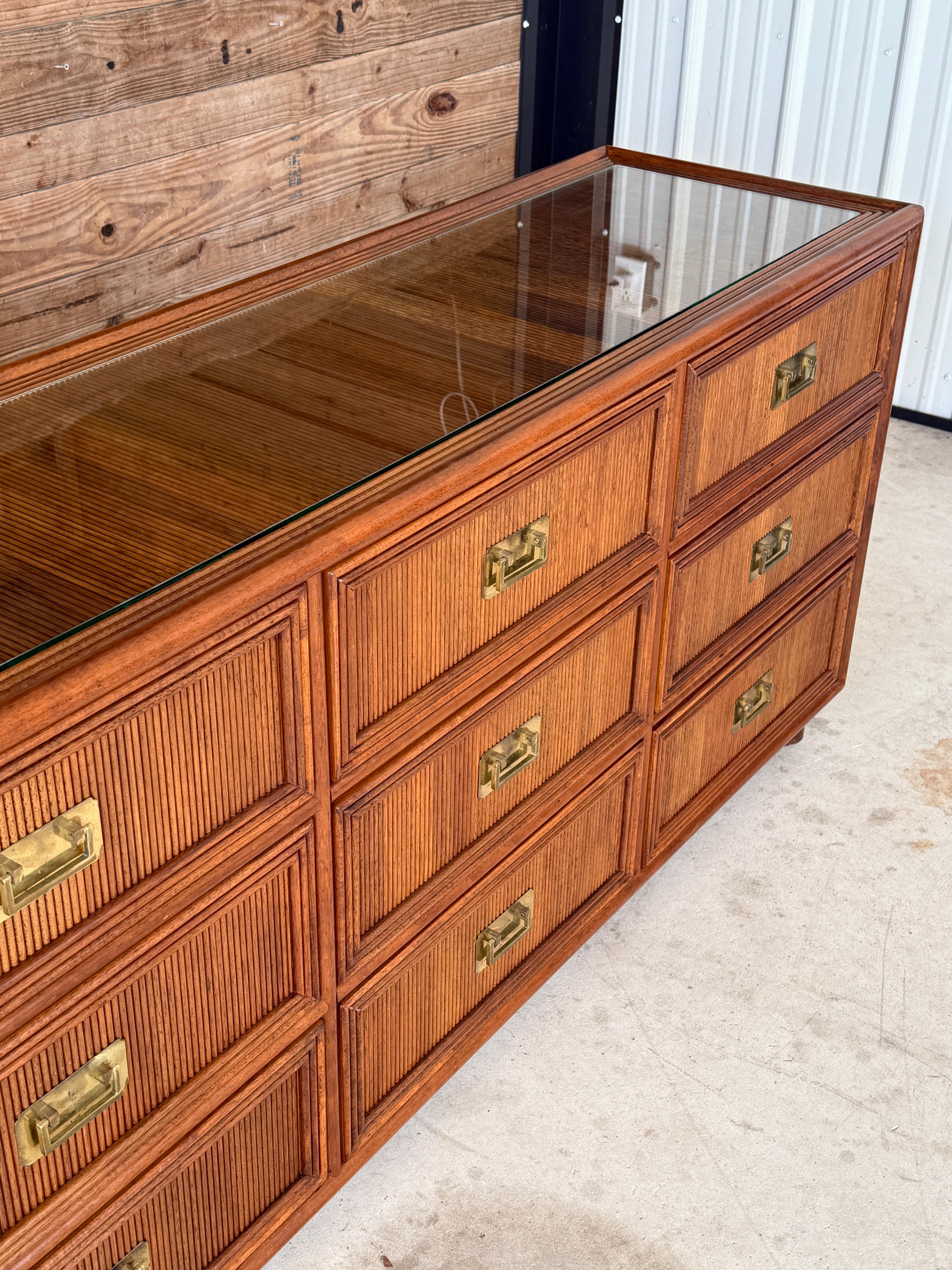 A timeless statement piece, this mid-20th century campaign-style dresser or sideboard showcases a refined design with tropical influences.
Crafted with rattan-wrapped panels and framed in hardwood, the piece features a striking reeded texture that