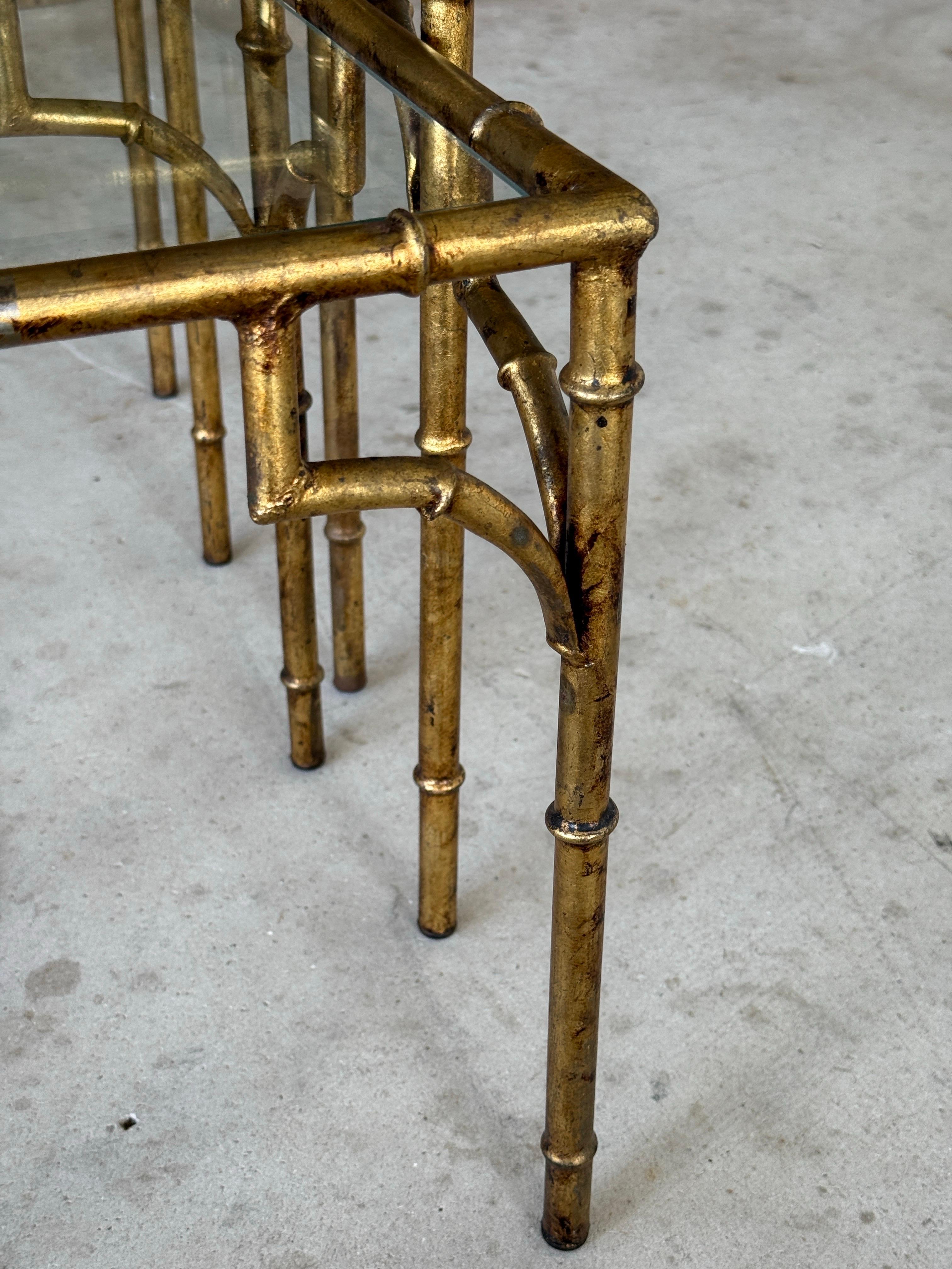 Un ensemble glamour de trois tables gigognes du milieu du 20e siècle dans le style Hollywood Regency, avec des cadres en métal dans un design de faux bambou avec une finition dorée vieillie. L'ensemble conserve son charme d'origine avec une patine