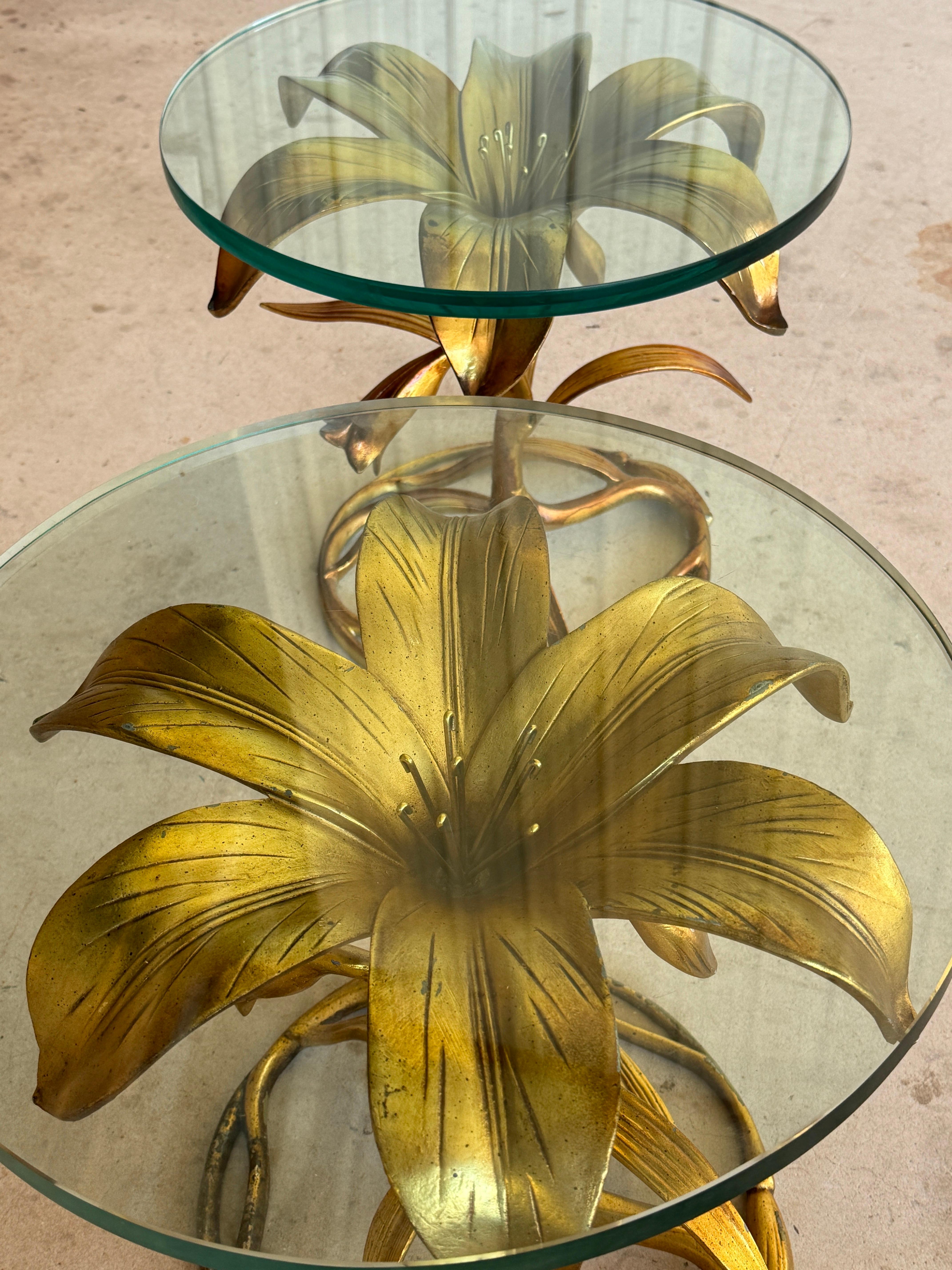 A sculptural pair of Mid-20th Century gilt lily flower side tables by Arthur Court. Each table features an intricately cast metal base with graceful stems, leaves, and blossoms supporting thick round glass tops. The design captures the natural