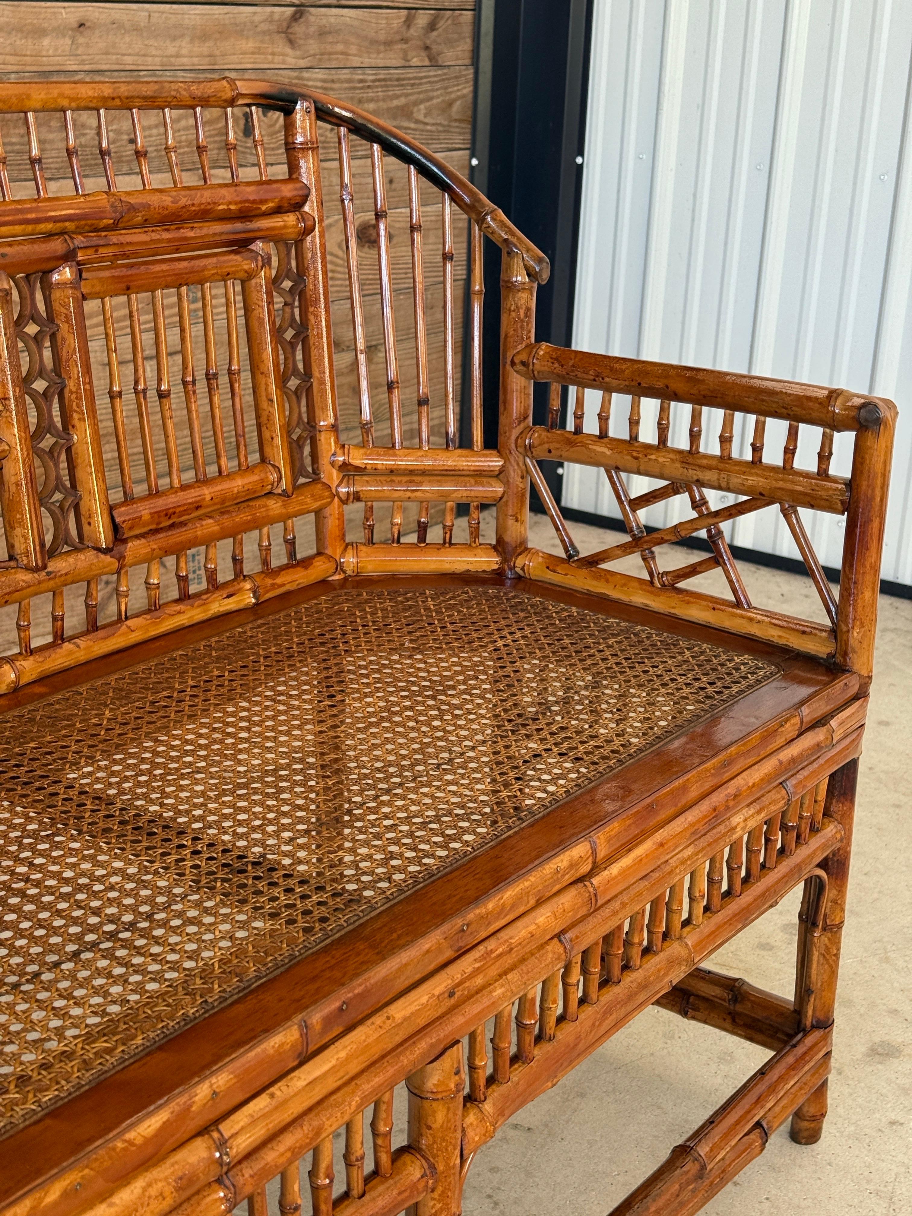 A beautifully restored Mid-20th Century bamboo settee in the Brighton Pavilion style, showcasing intricate fretwork and a warm honey-toned finish. The cane seat and architectural details lend an airy, coastal feel that blends seamlessly with