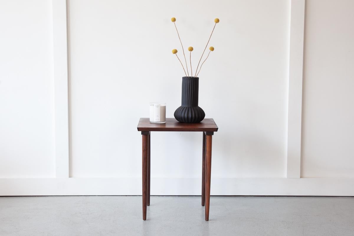 A sweet rosewood side table featuring a lovely grain on its top and long, elegant legs.