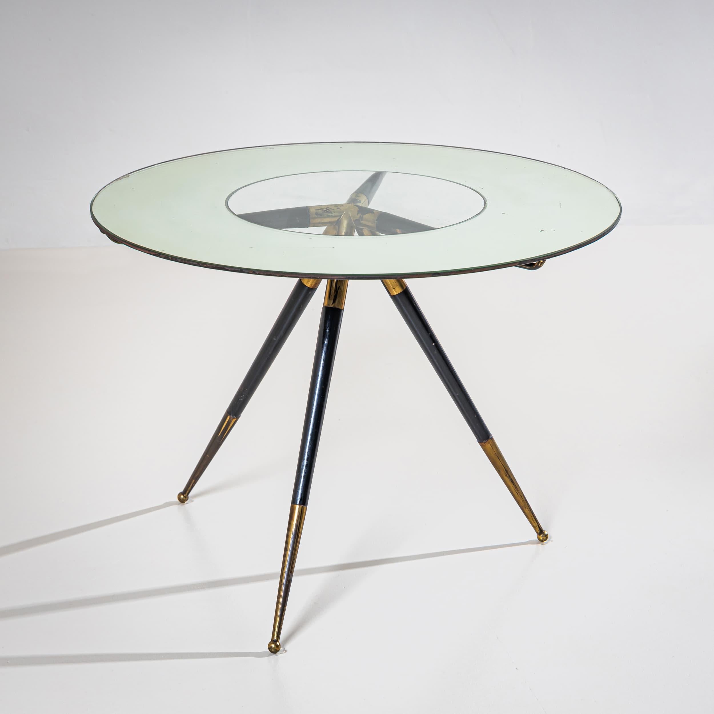 Italian coffee table with a round glass top featuring a frosted outer ring and a clear center, revealing the strikingly designed base. The structure includes brass elements and rests on three slender, tapered legs.