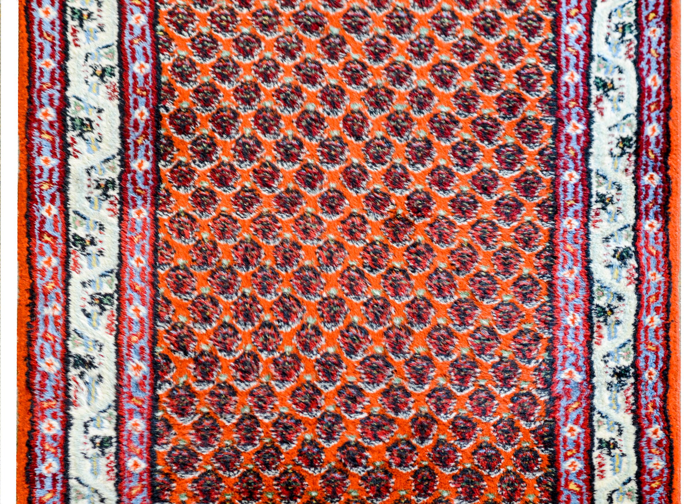 A monumental mid-20th century Indian Saraband runner of considerable length, with an amazing all-over paisley pattern on an orange background, surrounded by a wide border containing a wide central floral and vine patterned stripe flanked by two