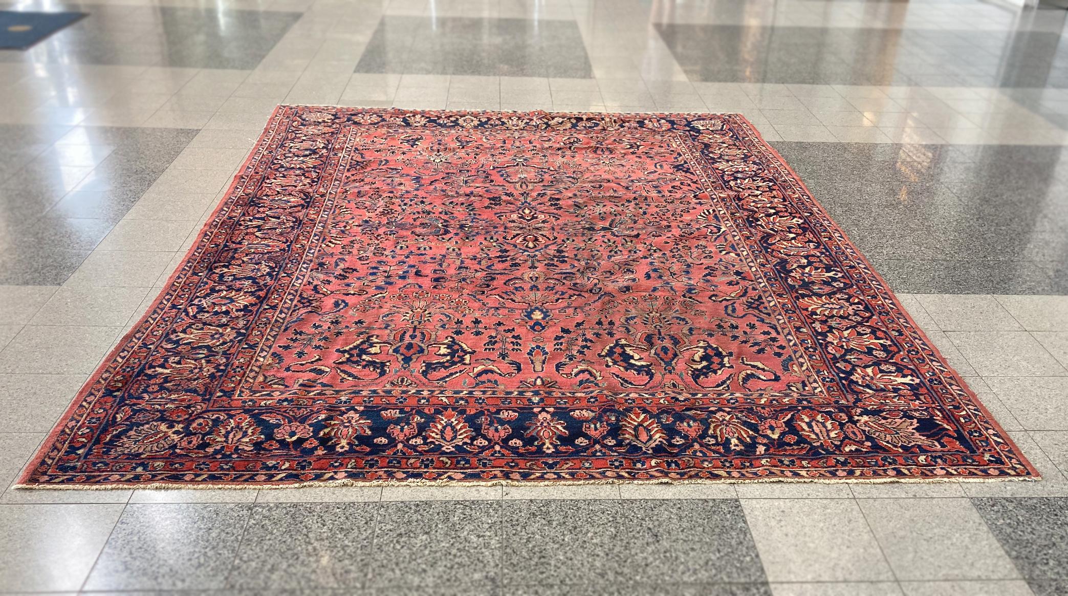 A richly hued Sarouk rug, handwoven, mid-20th century. The rug's palette is a beautiful arrangement of blues and gold on a red field. Floral and vine motifs fill the central rectangle, framed by a border of densely patterned blue and red bands. We