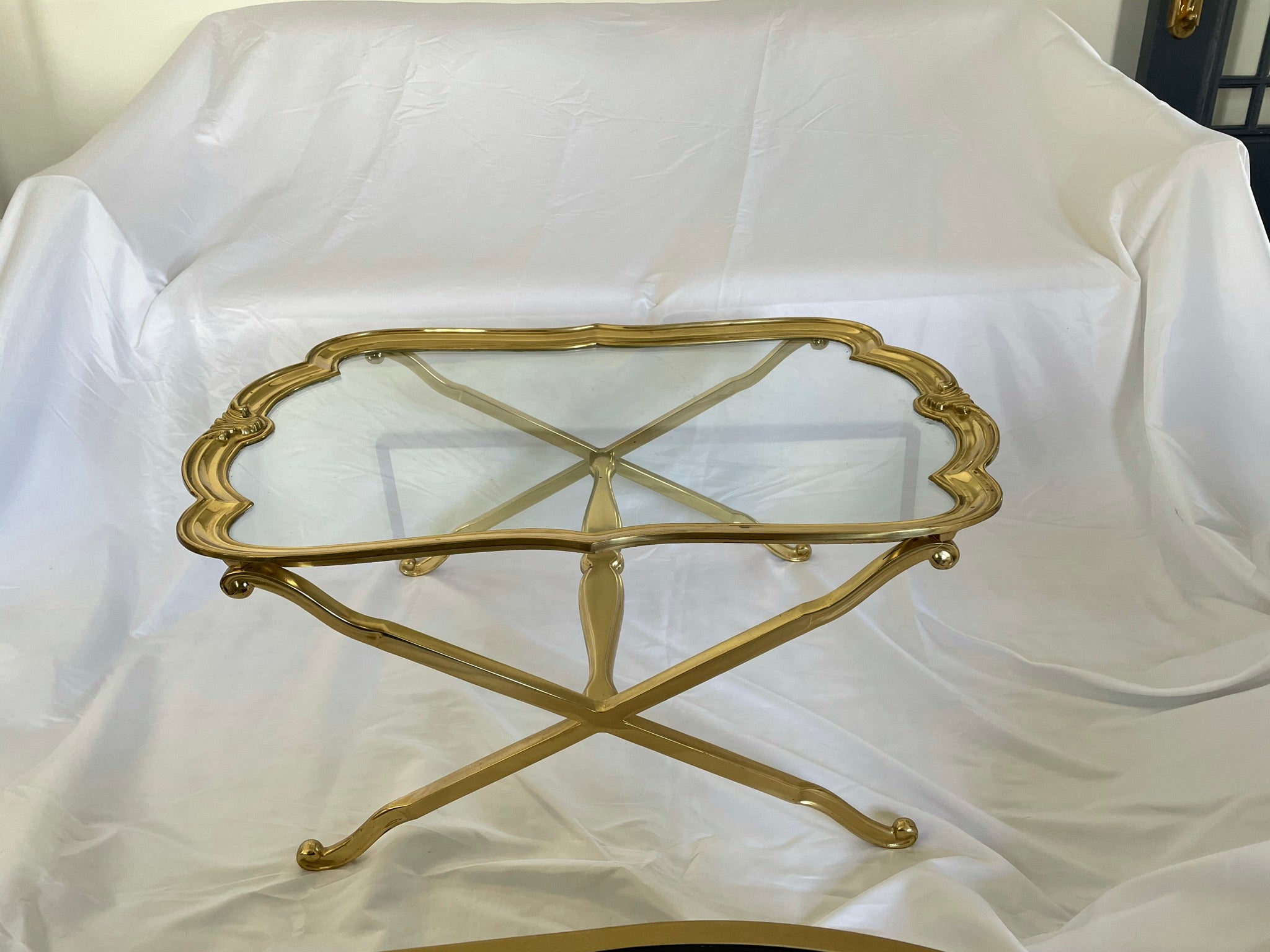Stunning brass and glass coffee or drinks table. Scalloped Edge glass top with fleur-de-lis detail. X base. Heavy. In the manner of Baker and LaBarge.