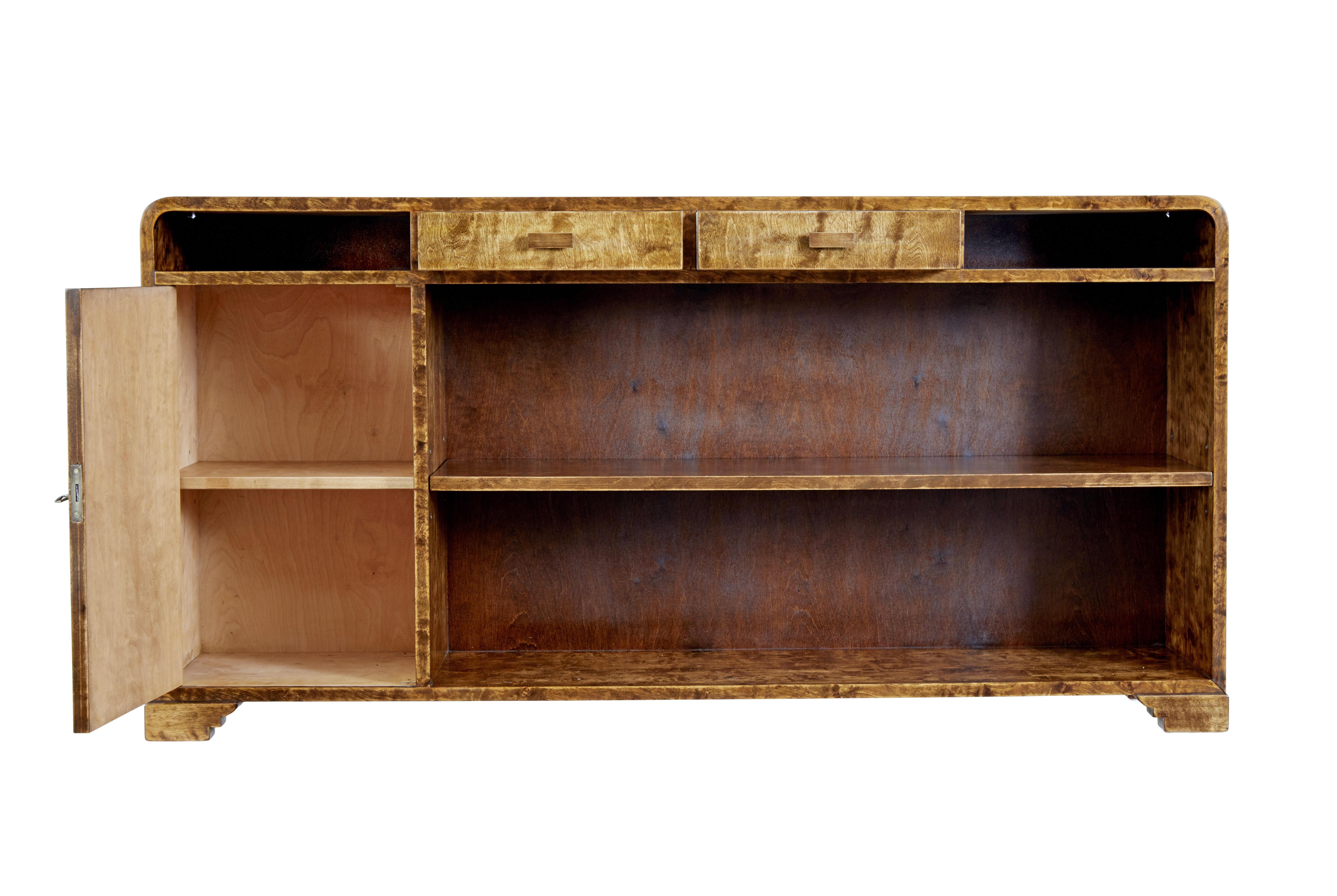 Mid 20th century Scandinavian birch bookcase by SMF Bodafors circa 1950.

Stunning burr birch low bookcase with rich golden colour. Shaped top with 2 drawers below the top surface and 2 open apertures for storage.

Single door cupboard to the