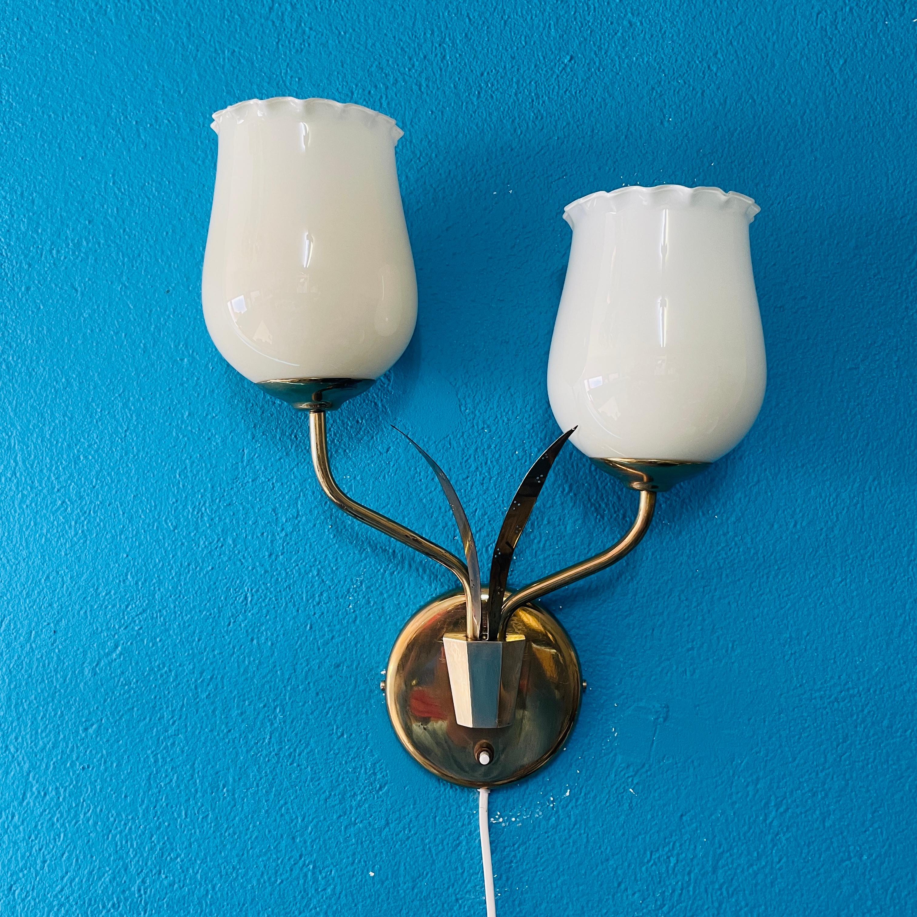 Vintage Brass Wall Lamp with Two Glass Shades – Paavo Tynell Style, Possibly manufactured by Itsu from Finland in the 1950's.

This mid-century modern brass wall lamp features two beautifully shaped opal glass shades that diffuse light softly,