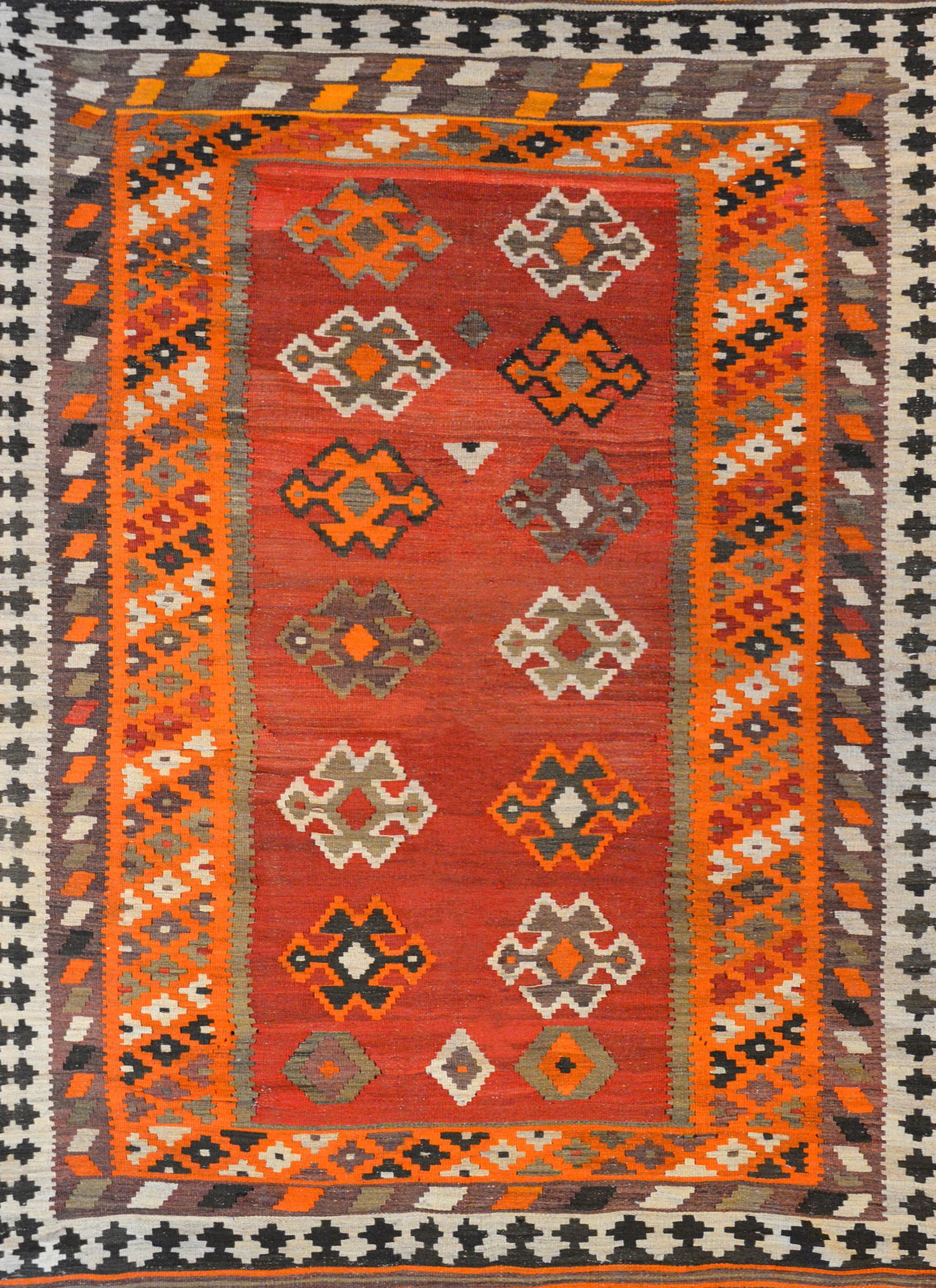 A wonderful bold mid-20th century Persian Shiraz Kilim rug with a fantastic pattern containing styled flowers woven in orange, white, grey, and black wool on an abrash crimson background surrounded by multiple petite geometric patterned stripes