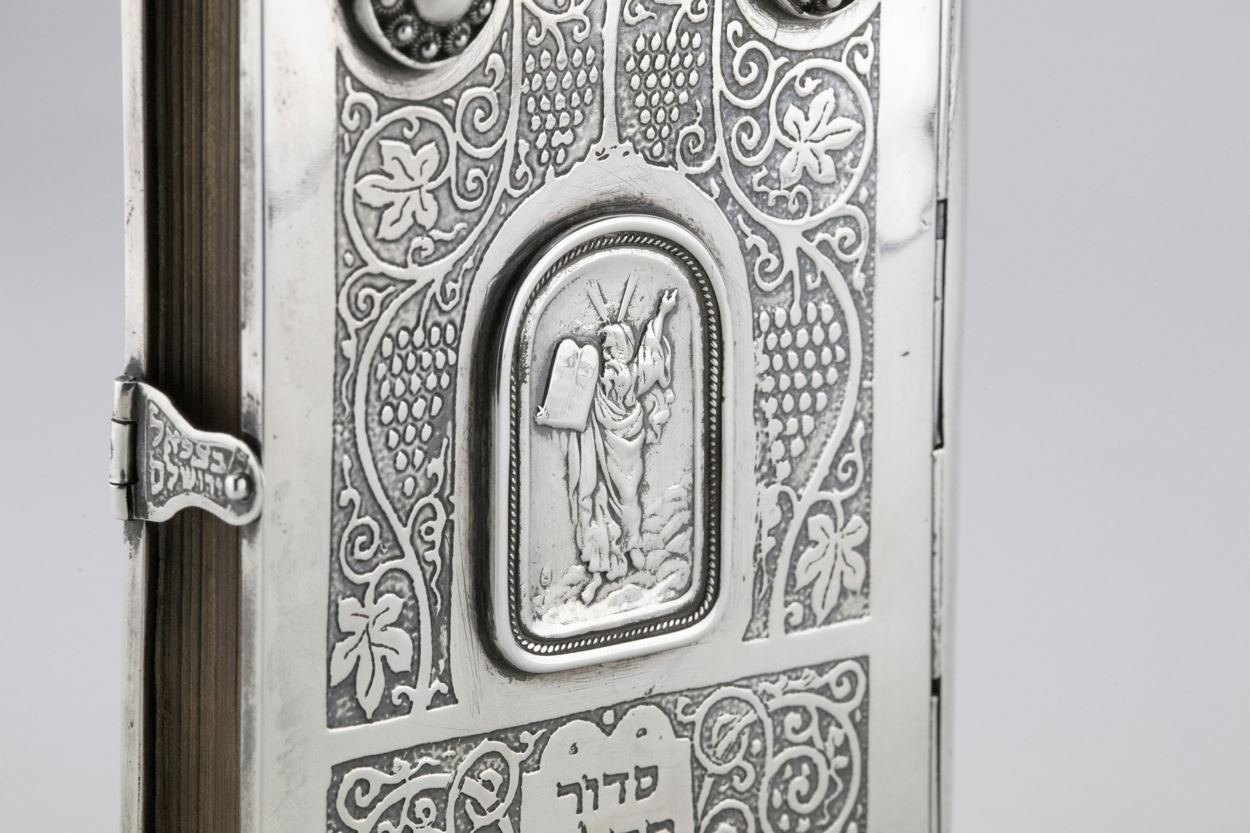 Sterling Silver book binding with the original Siddur by Bezalel school, Jerusalem, Israel, circa 1950.
On the front binding is a medallion showing Moses carrying the Tablets of the Law. Curving vine twigs and clusters of grapes are etched all