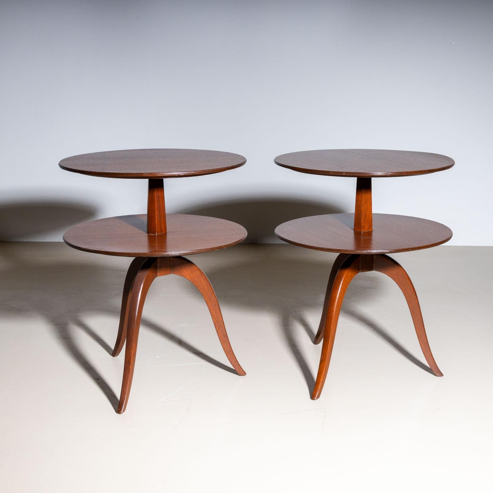 A pair of elegant side tables designed by Edward Wormley (USA, 1907–1995) for Dunbar, crafted in the mid-20th century. The wooden tables stand on three gracefully curved legs supporting a hexagonal central column. Each table features two shelves,