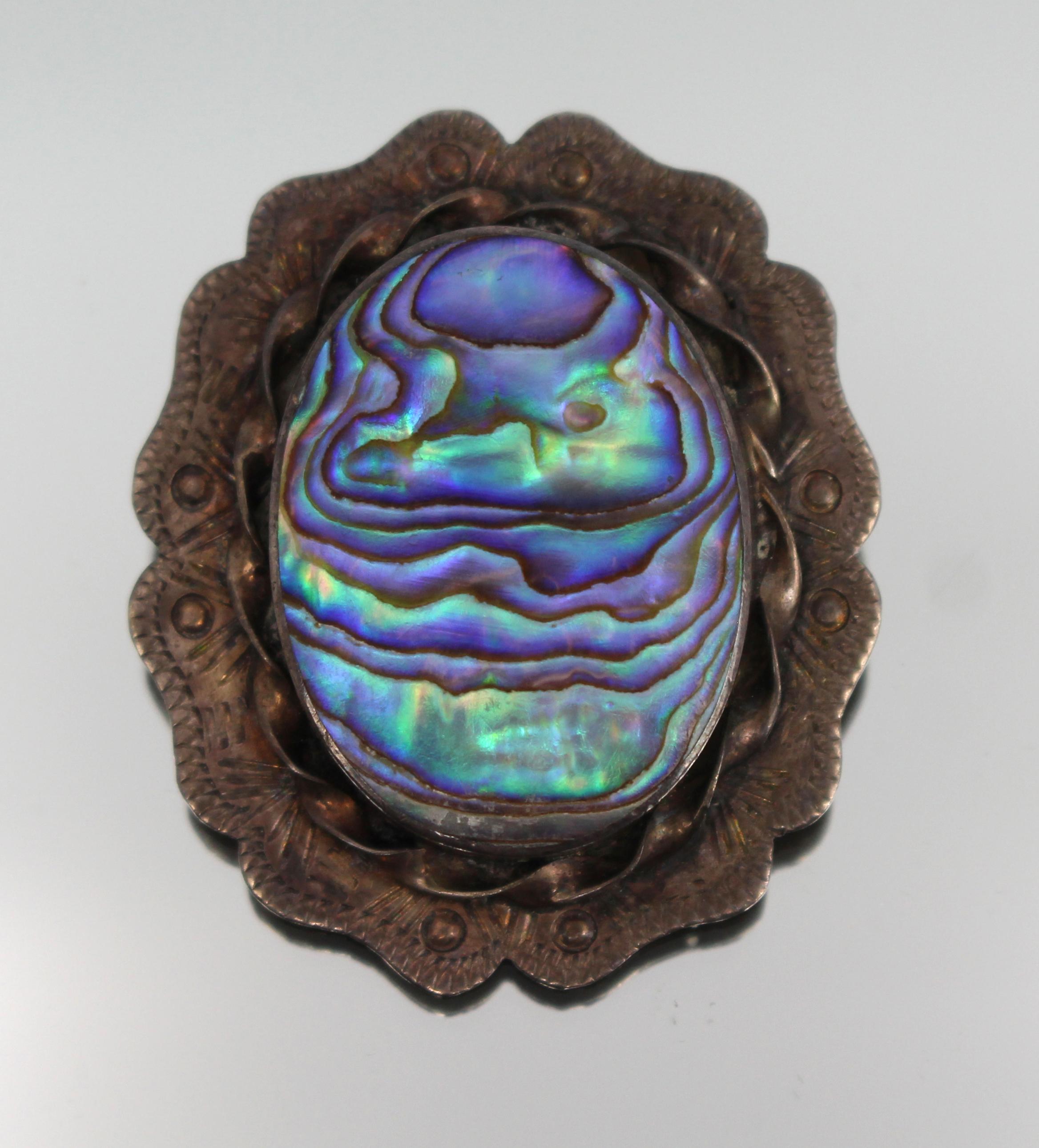 Mid 20th Century Silver and Abalone Brooch – c.1950

A nicely made mid-century brooch set with an oval abalone shell, mounted in a hand-tooled silver frame with scalloped edge and twisted border.

Marked to the reverse with rubbed 