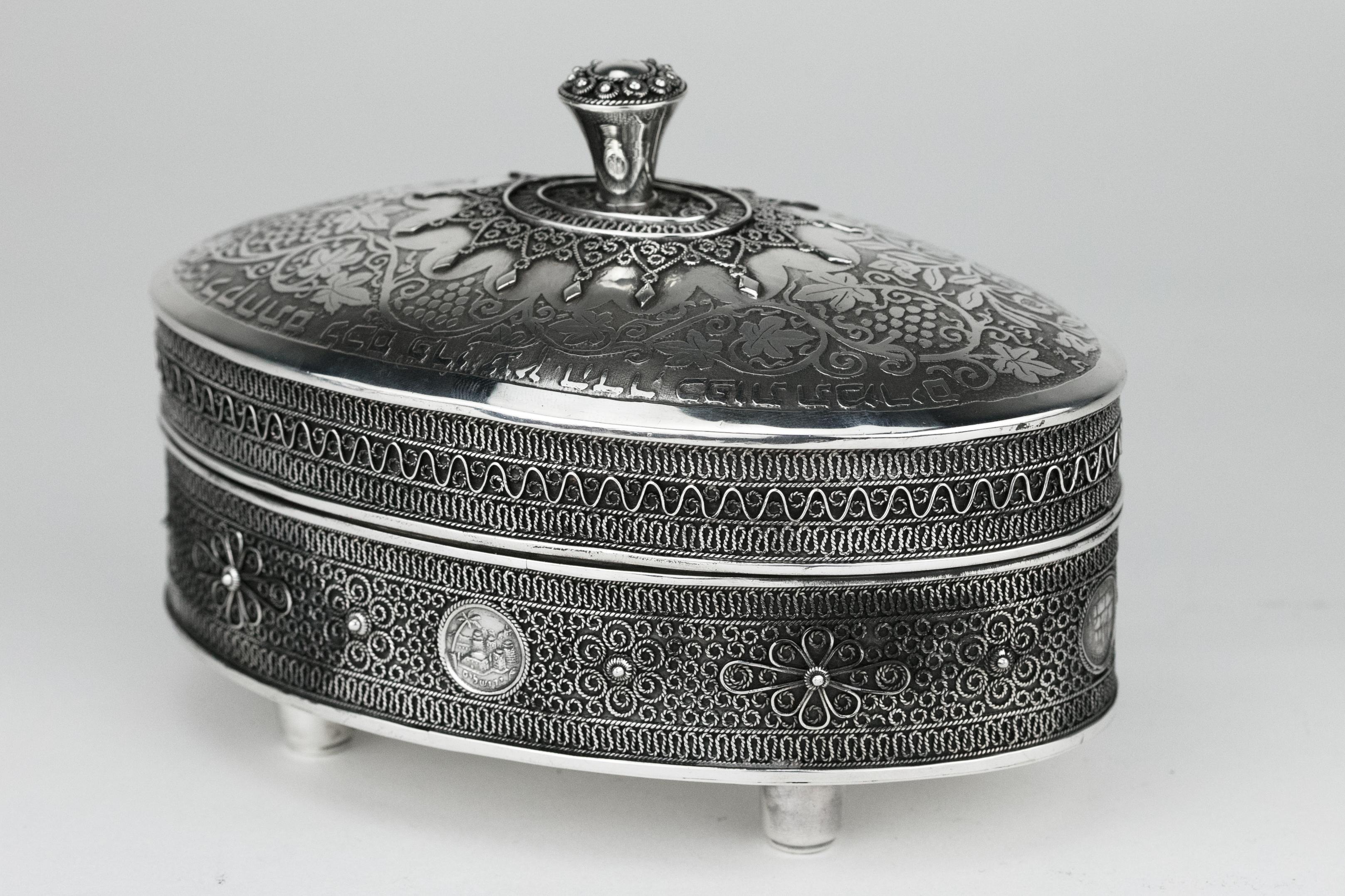 Silver and silver filigree Etrog container, Bezalel School, Jerusalem, circa 1950.
The lid is etched with grapes, vines, pomegranates and leaves, decorated with silver filigree on the finial, and around the finial, and inscribed in etched Hebrew