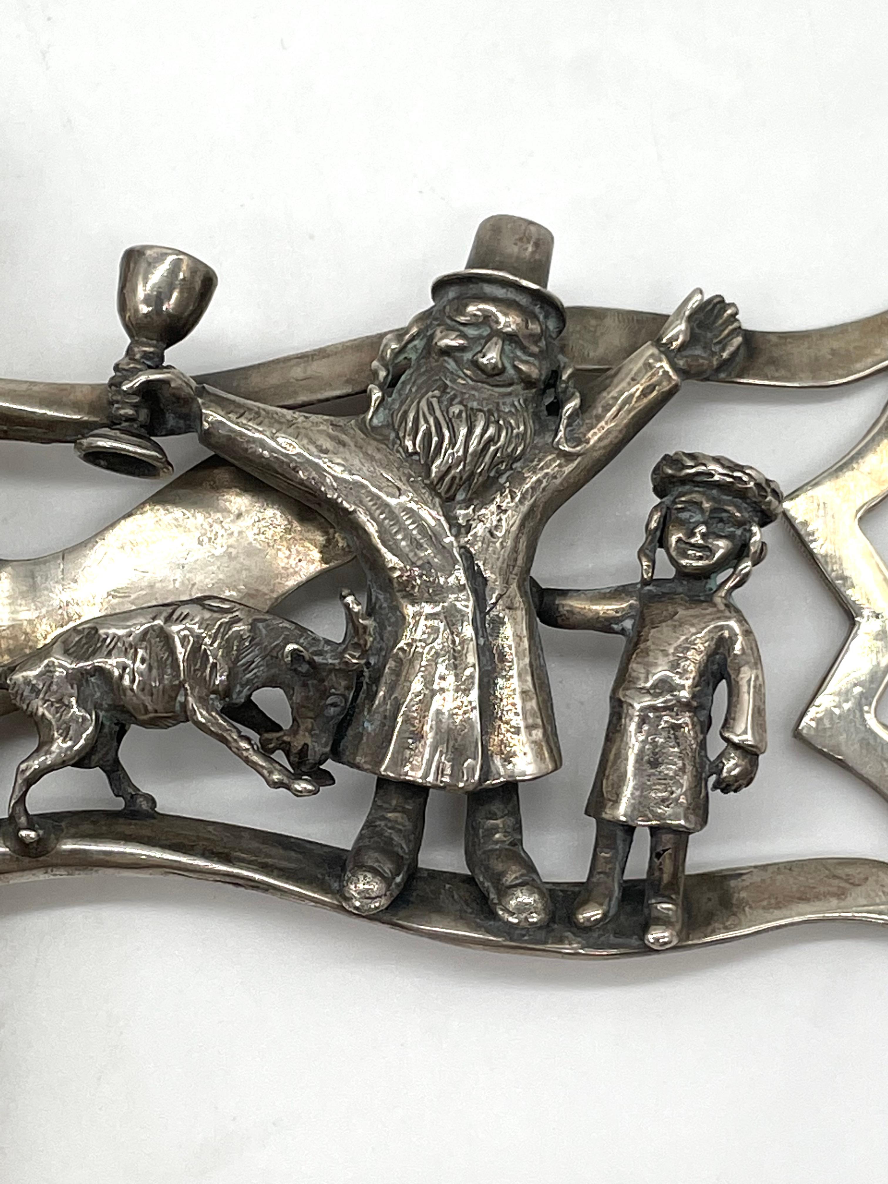 Mid-20th century silver grogger made by Peter Ehrenthal. Corresponding to the joyful spirit of the Jewish holiday of Purim, this grogger depicts a whimsical scene. At the center, three figures are joined in festive mood: a rabbi raising his hands in