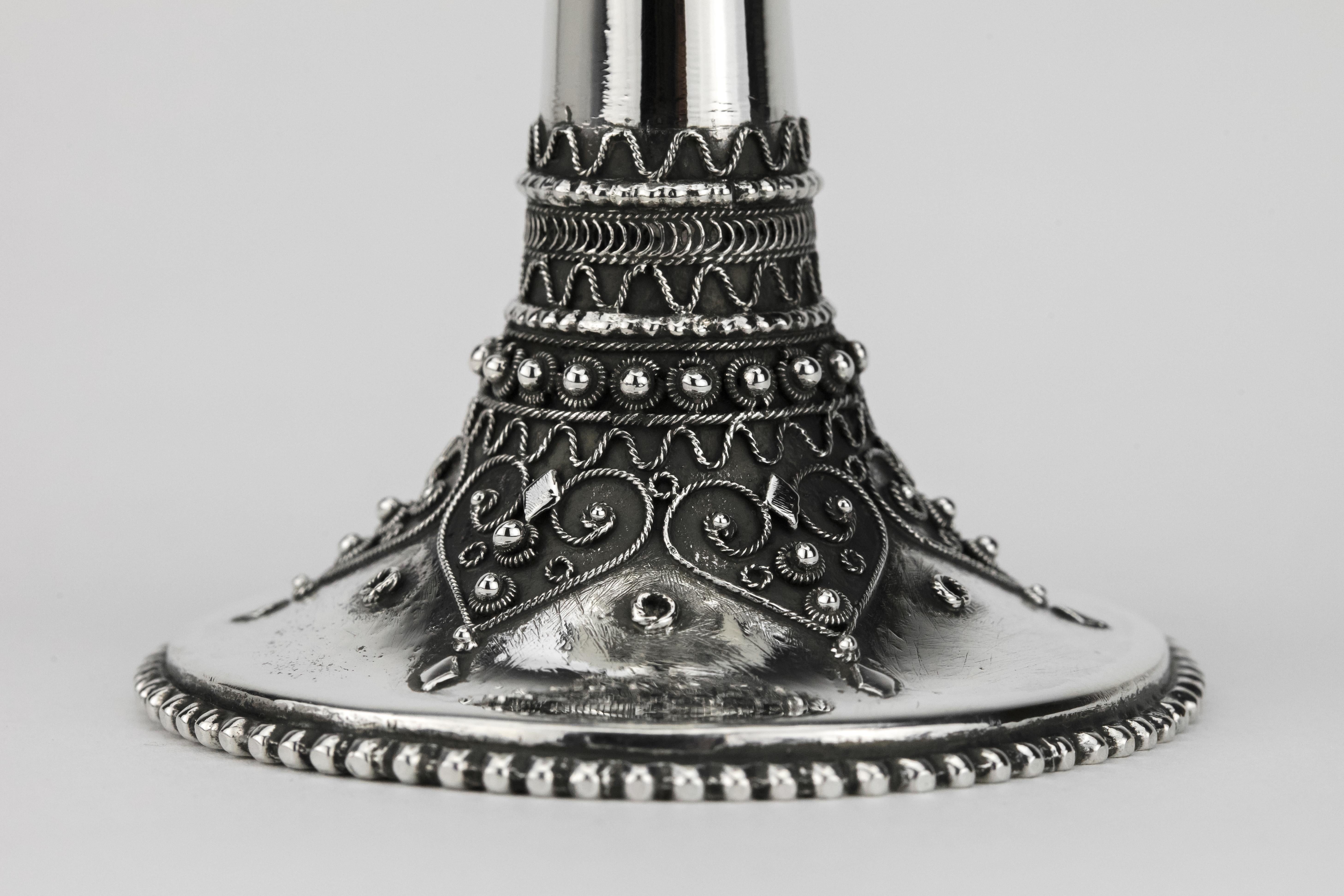 Handmade sterling silver Kiddush goblet by Bezalel School, Jerusalem, circa 1950.
On round base decorated with silver filigree and cut diamond shaped silver applications. The stem fitted with Bezalel insignia. The upper portion is acid etched with
