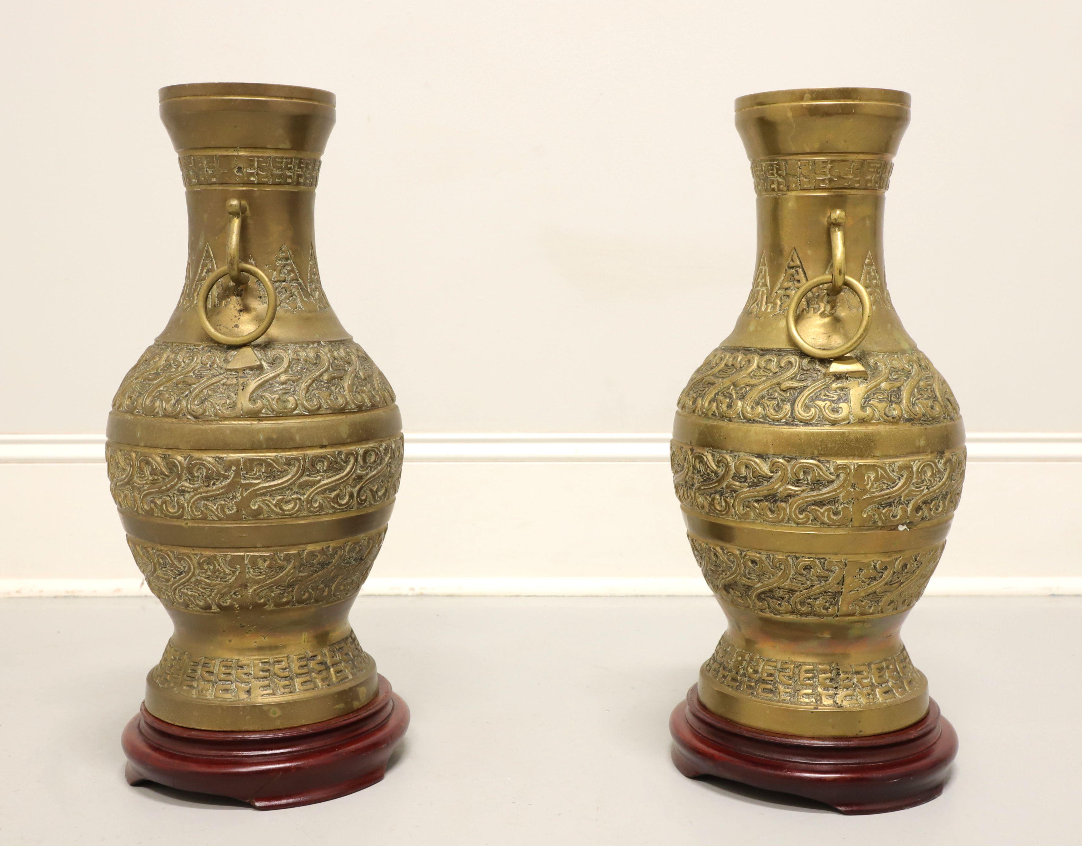 A pair of Asian style decorative brass urns, unbranded. Solid brass, hollow constructed, urns are decoratively adorned, have handles with rings and sit on unattached wood bases. Decorative use. Origin unknown, likely Asia, from the mid 20th Century.