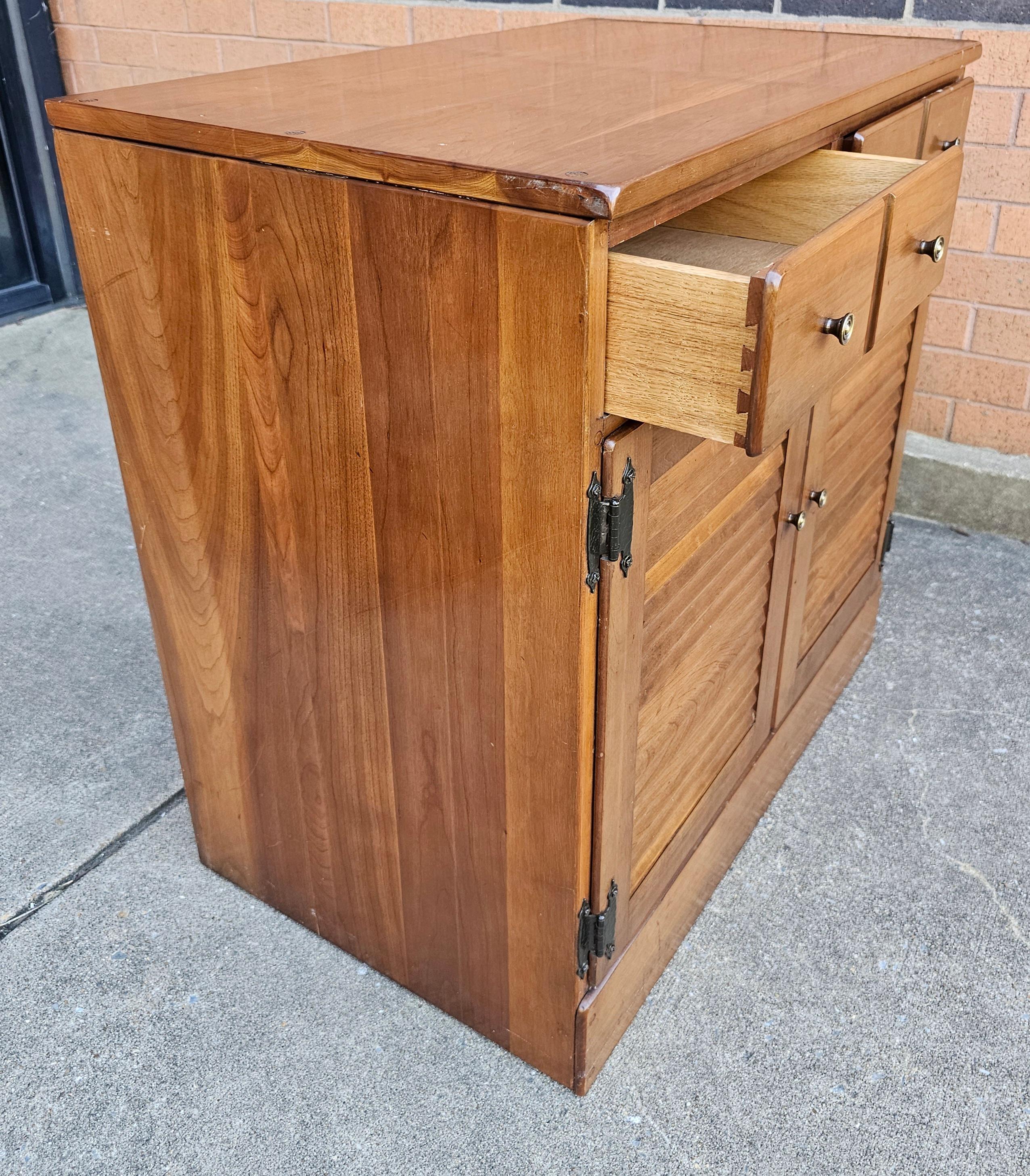 A Mid 20th Century Solid Cherry Side Cabinet, Circa 1970s. Features two top drawers and large double door storage cabinet with and an adjustable height shelf. Wood backing. Measures 30