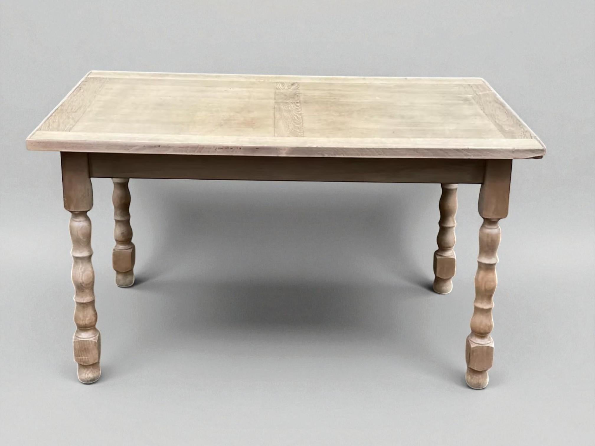 This understated yet sculptural farm table is crafted from solid oak and features a beautifully weathered, stripped finish that brings out the raw texture and grain of the wood. The tabletop displays subtle inlaid border panels, offering quiet
