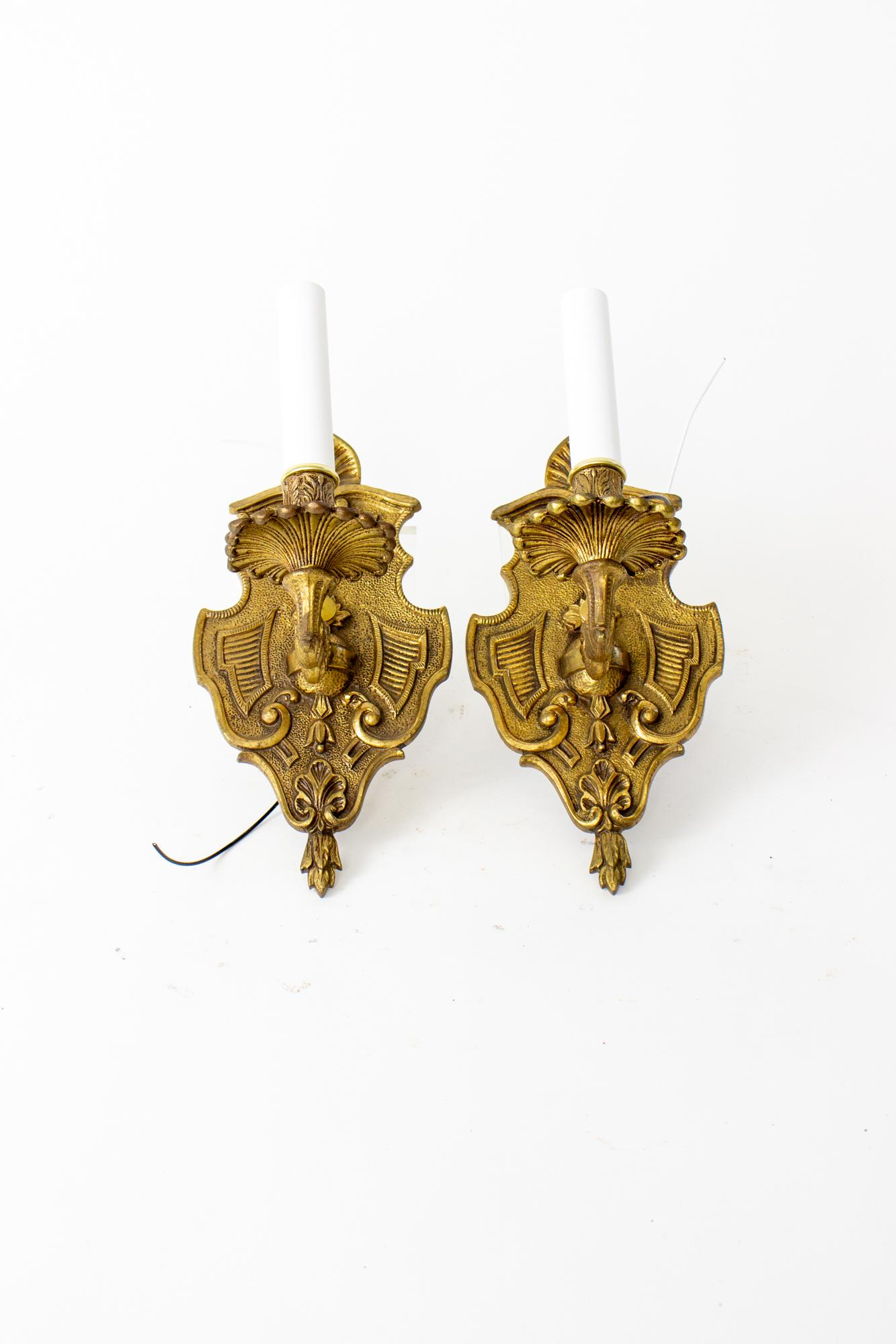 Mid 20th century Spanish cast brass sconces, a pair. Shield form backplate with a single ornate cast brass arm. Brass has a nice and even antique patina. Rewired with new candlecovers, ready for installation. Each sconce takes a single candelabra