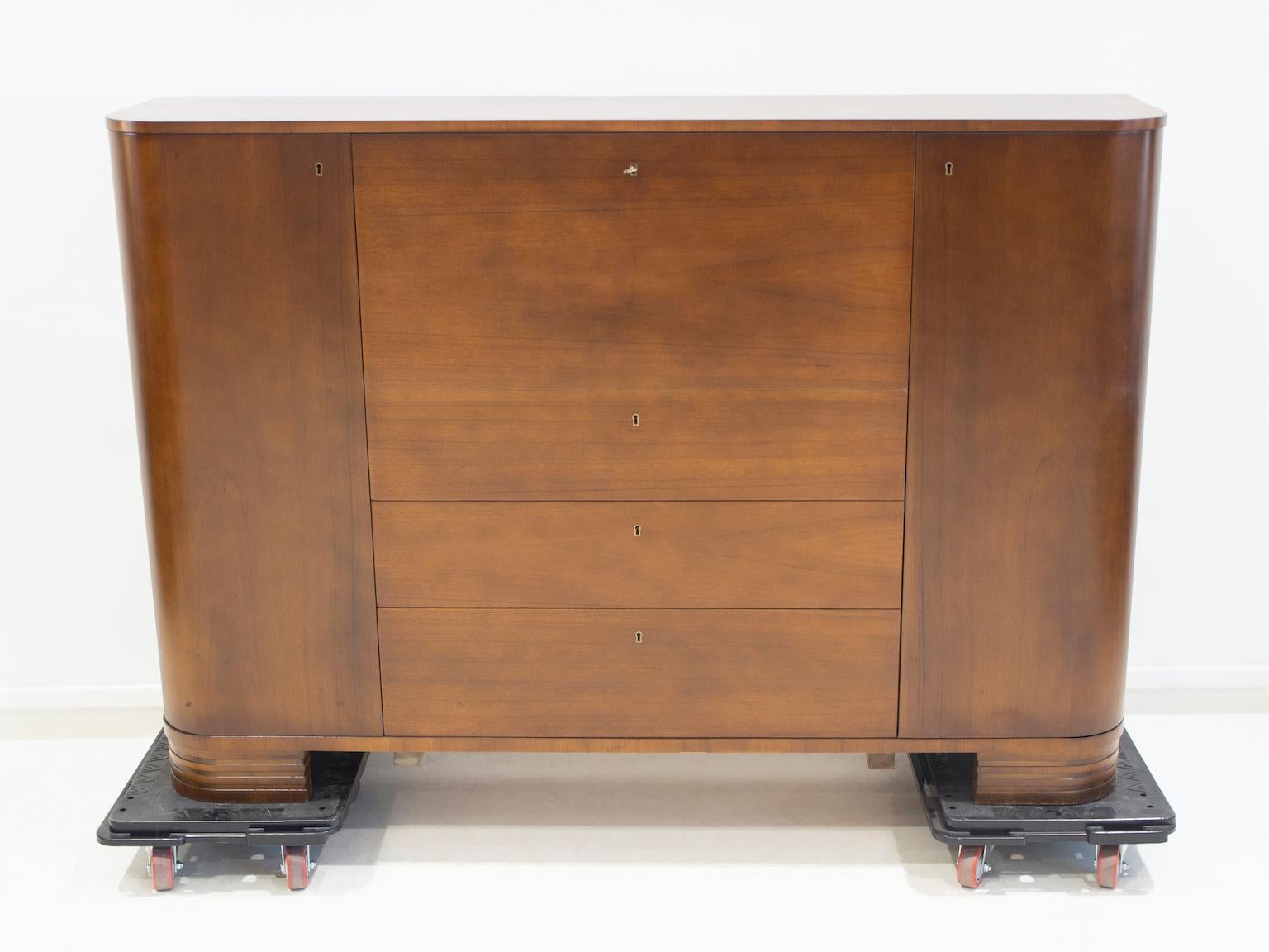 Swedish Modern style mahogany cabinet from circa 1940's. The two sides of the sideboard open up to reveal shelves. Three large drawers in the middle and a drop-down door on the top behind which are small drawers and shelves. Key included.