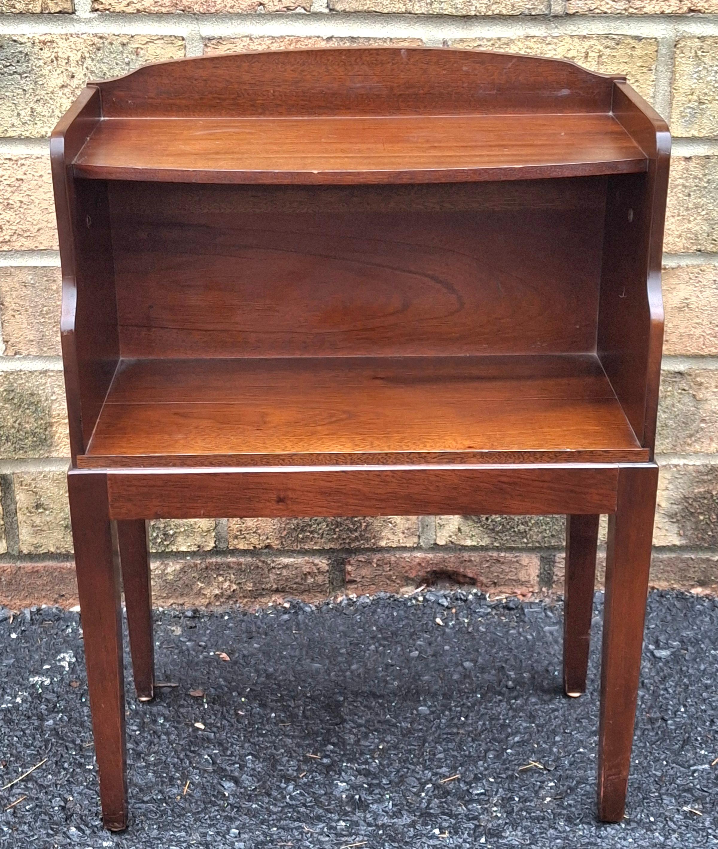  Table de chevet en acajou brun rougeâtre du milieu du 20e siècle. 
Le design comporte deux niveaux : une étagère ouverte au-dessus d'une surface inférieure, soutenue par quatre pieds élancés. 
Il est doté d'une poignée chippendale unique de couleur