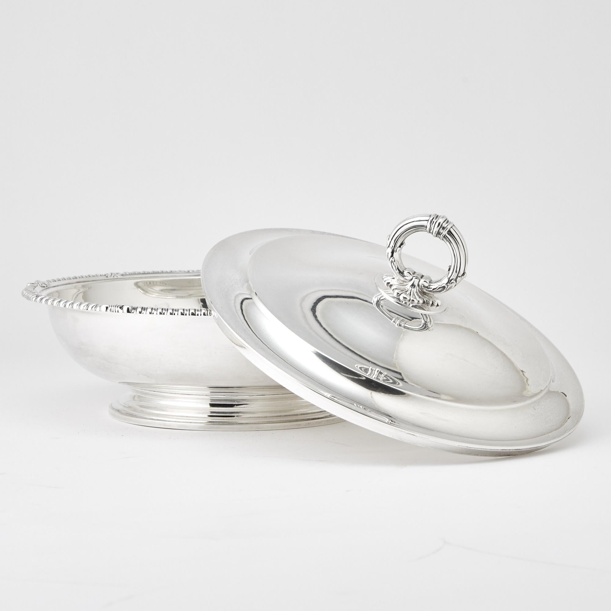 A stunning mid-20th century sterling silver covered tureen by the renowned Tiffany & Co., showcasing the timeless elegance of Art Deco design. This exquisite piece features a classic circular form adorned with intricate shell and gadrooned border