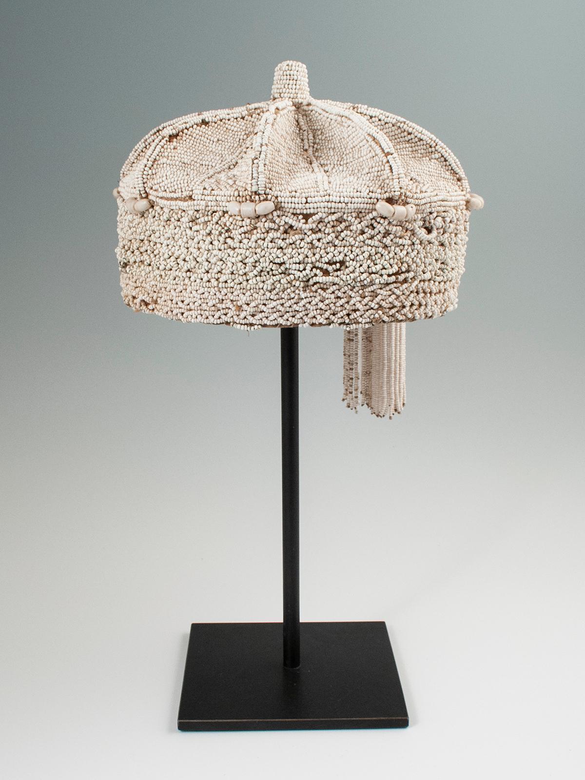 Mid-20th century tribal white beaded crown, Yoruba people, Nigeria

A lovely example of a chief's white beaded crown with two tassels hanging on one side, some slight bead loss and a small area of bead replacement. Custom base included. Size: 8?