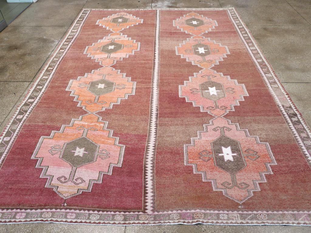 A wool pile of symmetric knots on a cotton foundation, signed by the weavers Yilmaz and Sidik. The open rust-red field is divided vertically, with each half displaying a pole medallion of four strongly stepped salmon-colored diamonds, each with a
