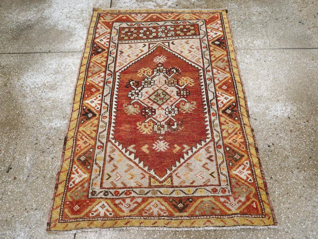 Ein türkisch-anatolischer Teppich im Vintage-Stil. Ein Rautenmedaillon mit Nelkenumrandung befindet sich auf einem roten Feld in einer mehrfarbigen Umrandung aus abwechselnden Dreiecken und abstrakten Blumen. Oberhalb des Feldes befindet sich ein