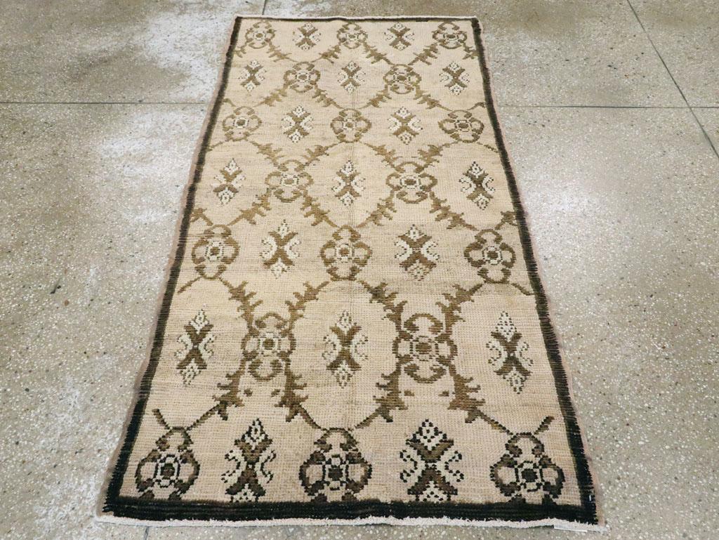 Un tappeto turco anatolico vintage. Il fondo sabbioso avorio abraso di questo spargimento rurale turco mostra un reticolo di foglie rotonde e concave tre a tre che racchiudono forme di rosette astratte bianche e marroni con fiori quadrilobati più