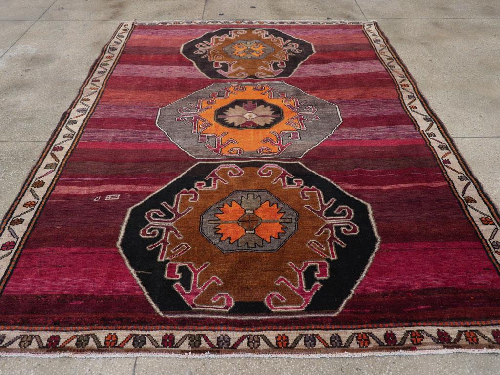 This piece features a wool pile of symmetric knots on a wool foundation. Smaller than most vintage Kars carpets, it boasts a boldly simple design. The abrashed burgundy-red field is divided into panels and lines, adorned with three nearly touching