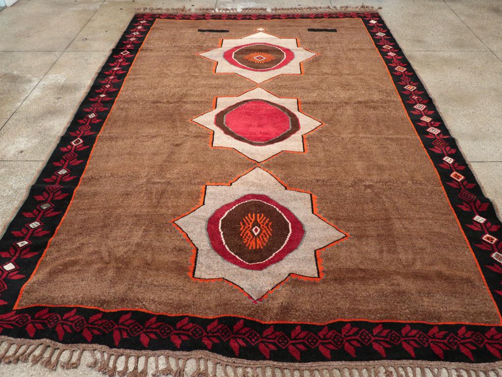 Cette pièce présente une pile de laine composée de nœuds symétriques sur une base de laine. Trois octagrammes écrus audacieux défilent au centre du champ brun moyen abrasé, chacun entourant un motif de disque focal presque circulaire. Chaque