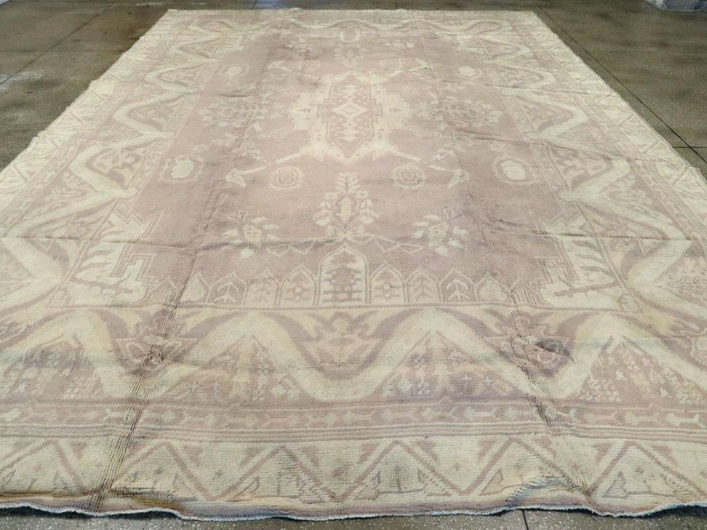 A vintage European Oushak large carpet. The light colors of this decorative Oushak belie the wild central cartouche medallion with its bird head diagonal corner extenders and the undulating snake pattern of the main border. Soft and bold, subdued