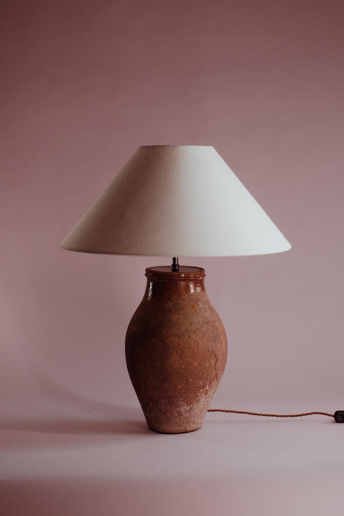 Cette jarre turque vintage en terre cuite présente un col émaillé distinctif qui contraste magnifiquement avec son corps texturé et terreux. Elle était traditionnellement utilisée pour conserver les céréales et les provisions essentielles. Cette