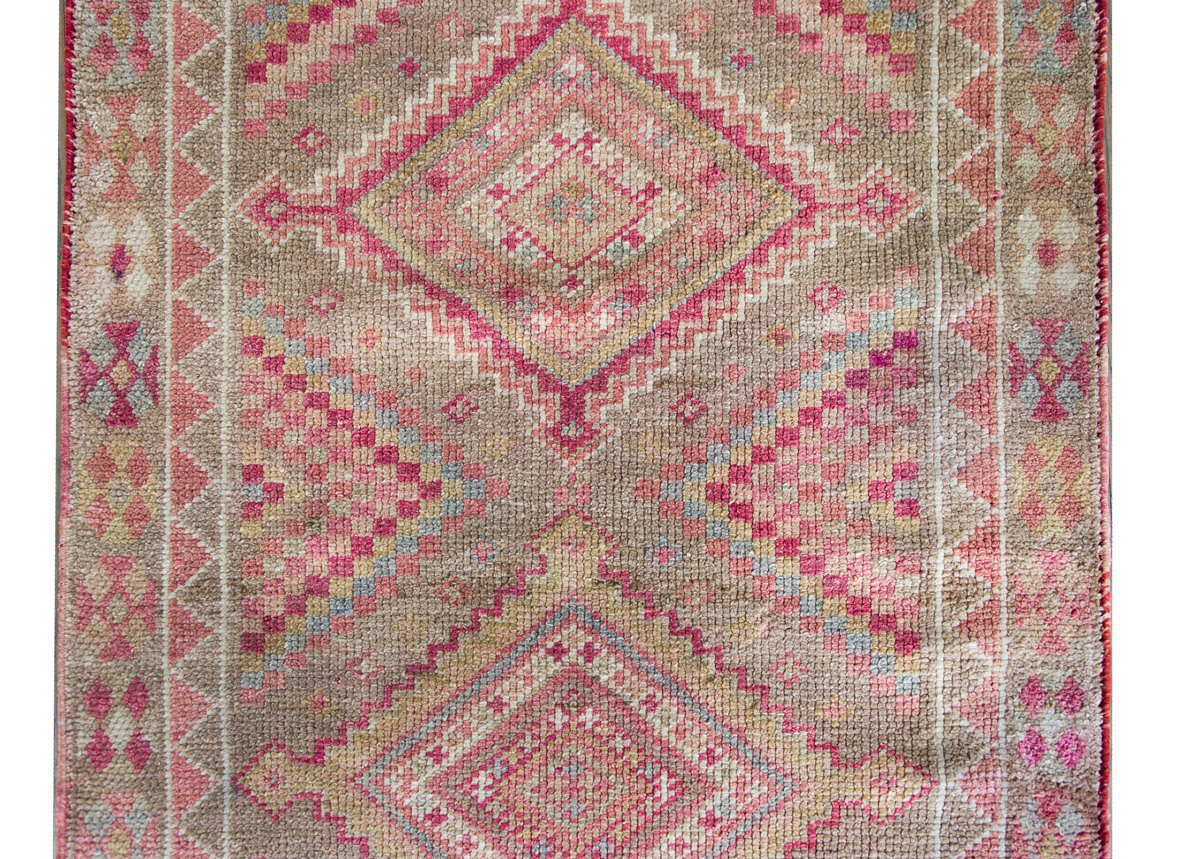 A stunning Mid-20th Century Turkish Konya runner with a simple all-over diamond pattern woven in the most wonderful color palette of pastel pinks, indigos, golds, and oranges, and set against a natural undid brown wool ground, and surounded by