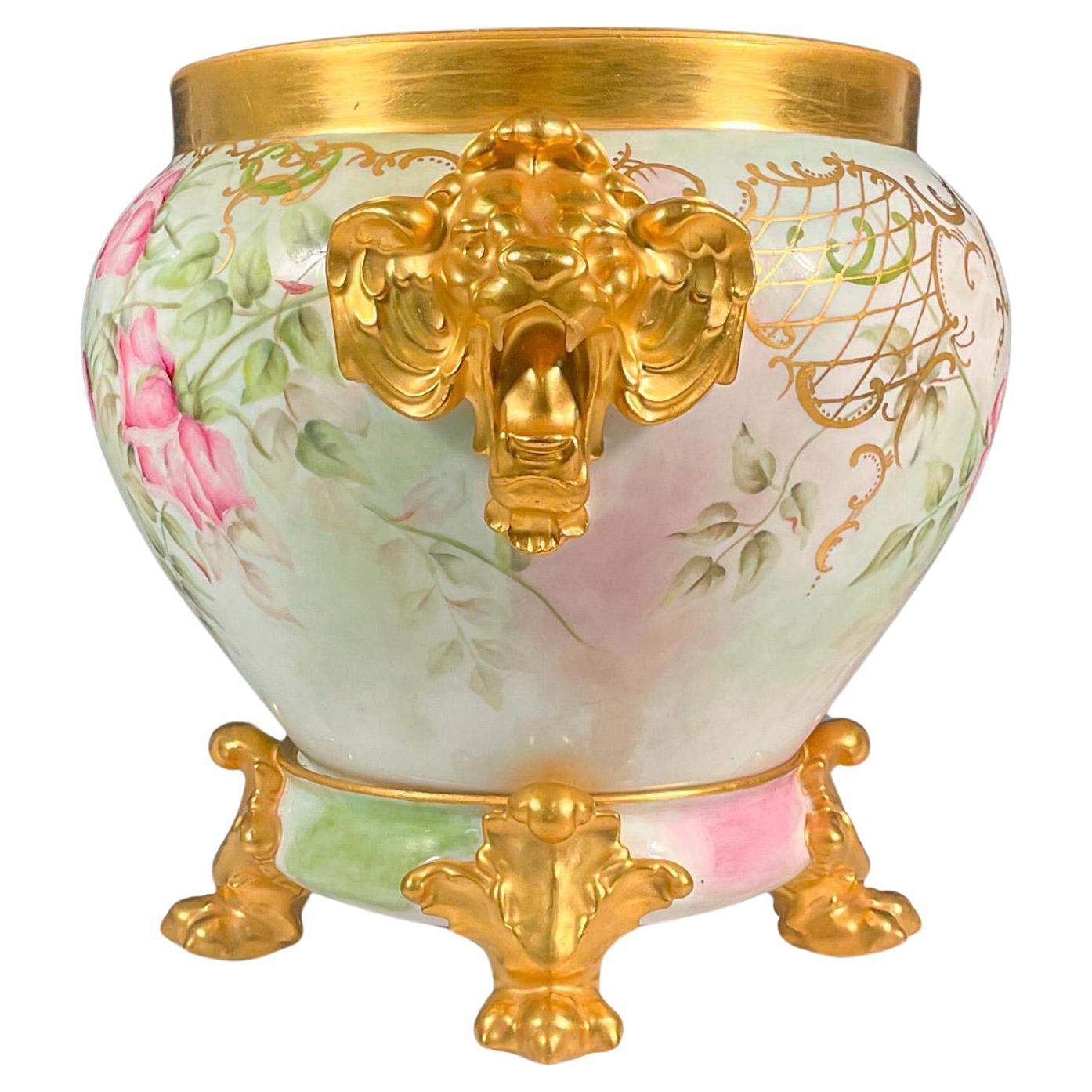 Presenting an exquisite Mid 20th Century Limoges porcelain jardiniere and stand set. This two-piece ensemble features a stunning white, pink, and green-toned planter, adorned with luxurious gold accents. Gold lion head handles are positioned on