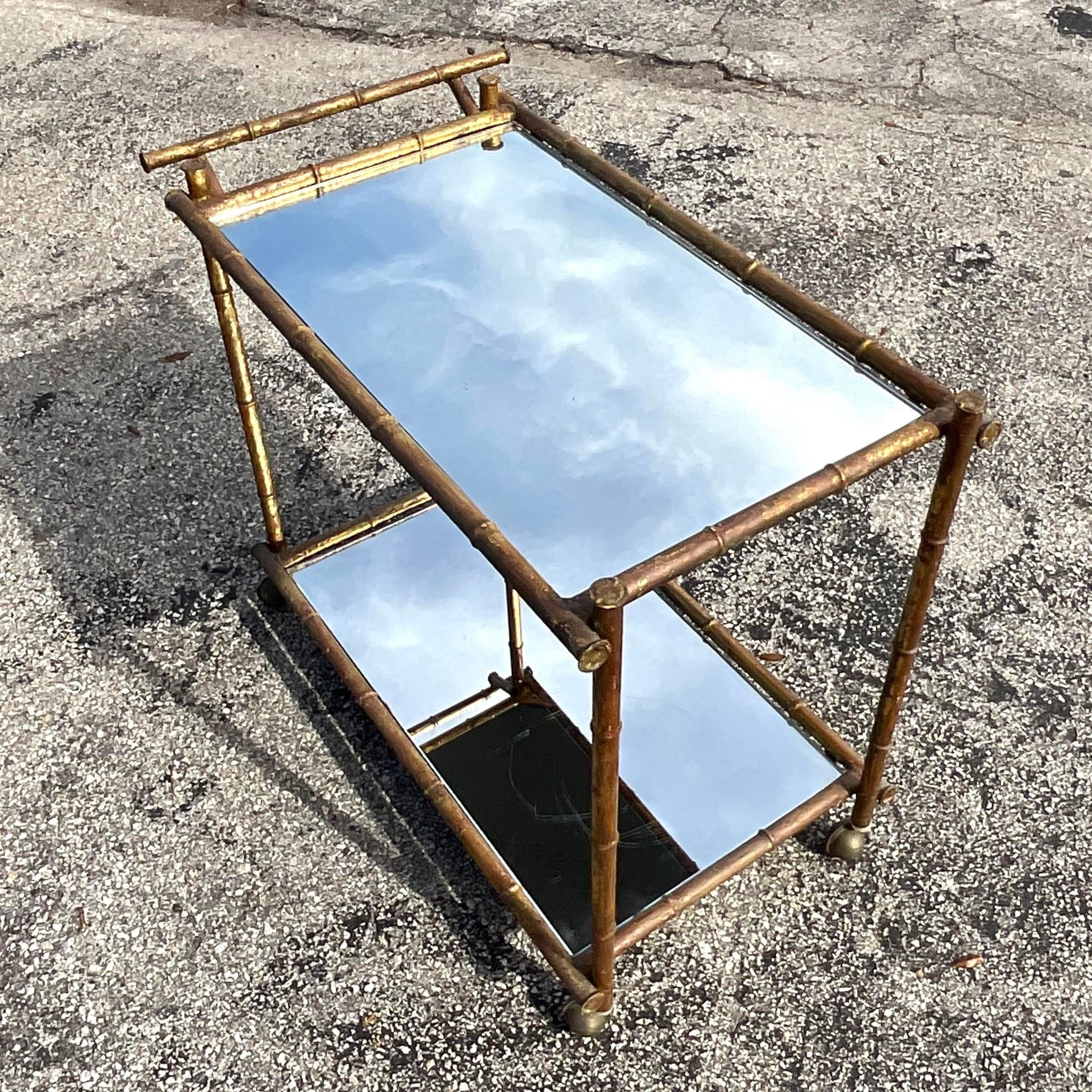 A stunning vintage Coastal bar cart. A chic metal bamboo frame with a patinated gilt finish. Inset mirrored shelves. Acquired from a Palm Beach estate.
