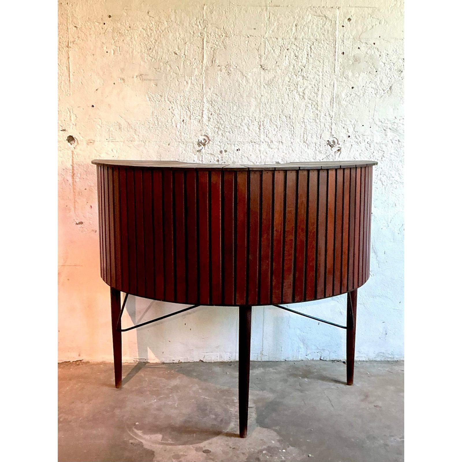 Elevate your entertaining with this exceptionally stylish vintage Mid-Century Modern dry bar. Its captivating demi-lune shape is beautifully accentuated by a rhythmic facade of vertical hardwood planks, showcasing a rich, warm grain and superb