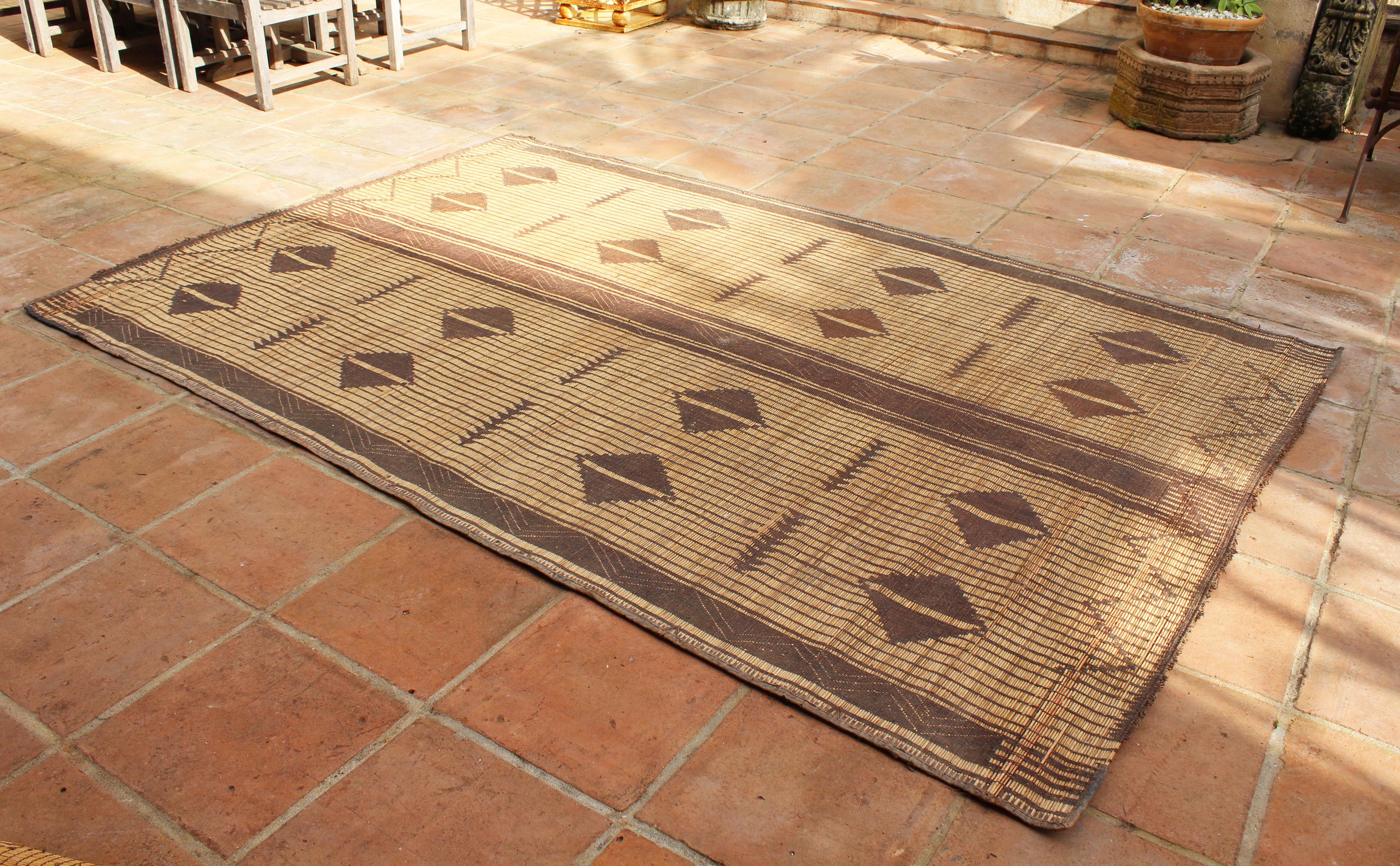 Moroccan Tuareg leather mats are made of dwarf palm tree fibers and handwoven with leather stripes, this are great to use indoor or outdoor, beautiful brown earth-tone colors. This vintage midcentury carpets are made in the desert of Morocco near