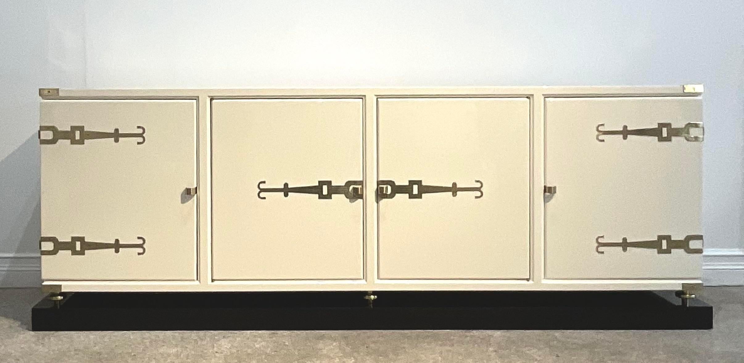 A vintage Regency Monumental credenza. Designed by the iconic Tommi Parzinger for Parzinger originals. Unmarked. A beautiful original White chocolate lacquered with heavy brass buckle hardware. Rests on a black lacquered plinth. Acquired from a Palm